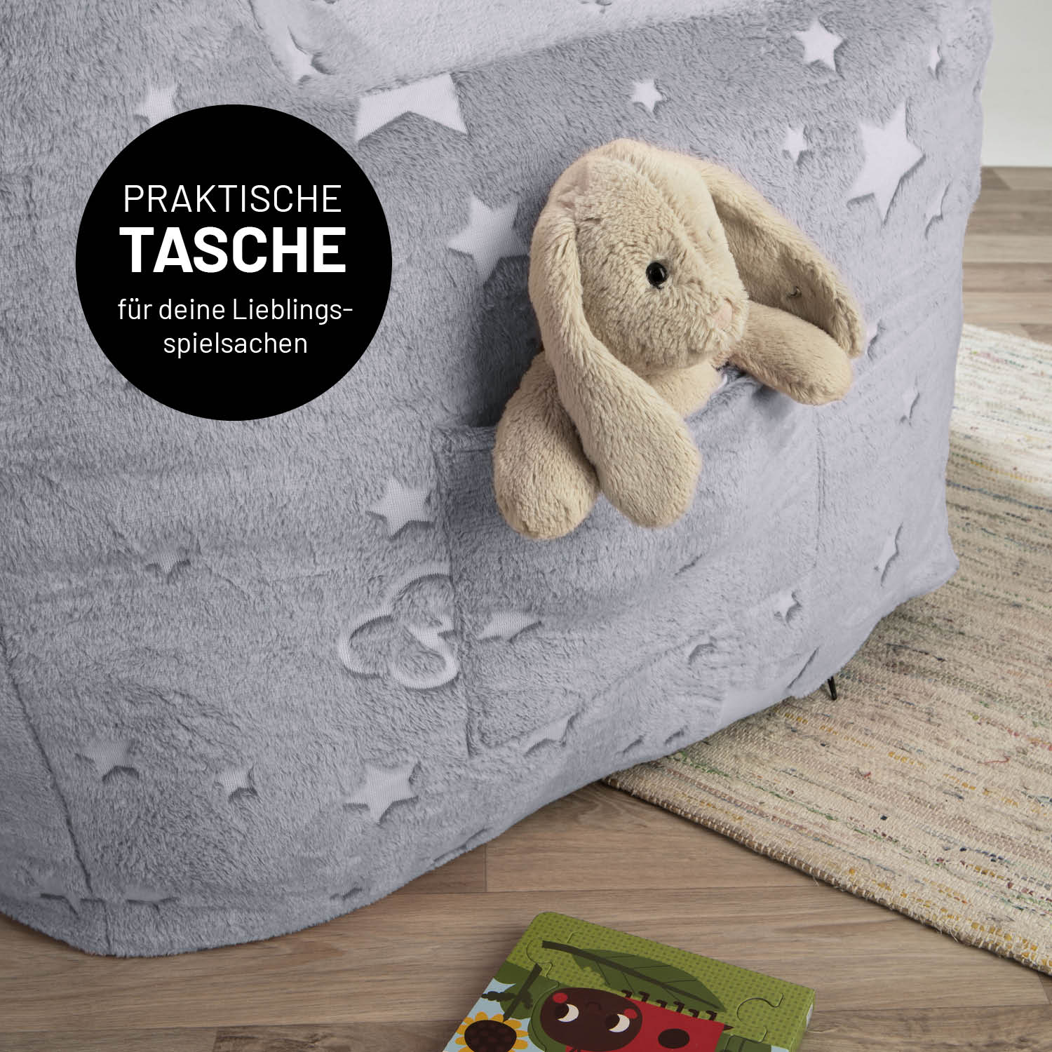 Ein Kuscheltier-Häschen in der praktischen Tasche des grauen LUMALAND Kinder-Sessels "Glow in the Dark".