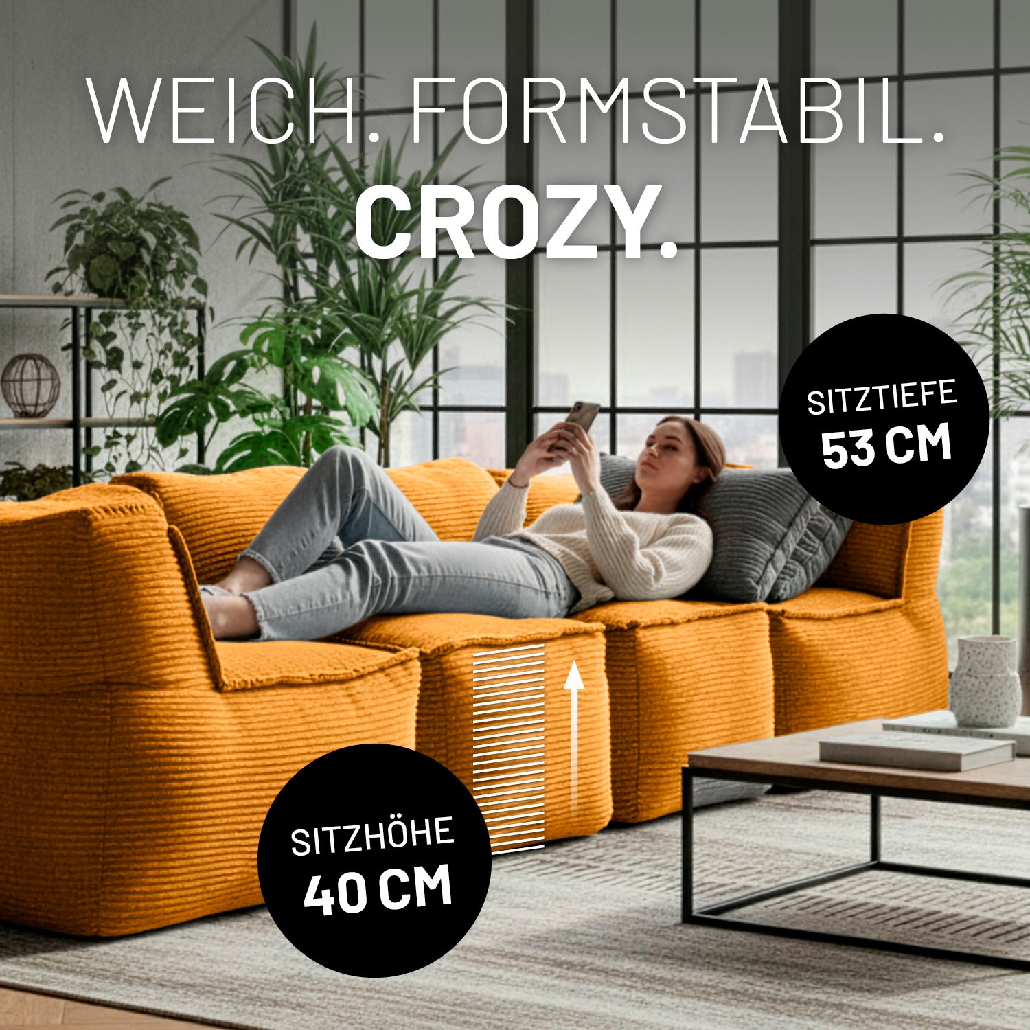 Modulare senfgelbe Lounge-Sitzlandschaft mit 40 cm Sitzhöhe und 53 cm Sitztiefe, auf der eine Frau entspannt liegend ihr Smartphone nutzt.