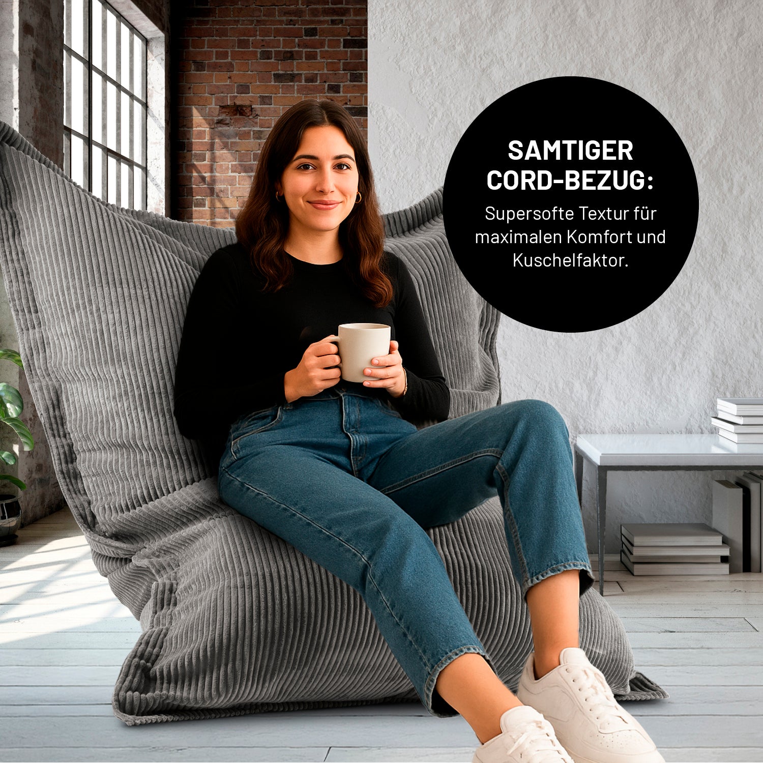 Eine Frau mit Kaffeetasse sitzt in einem Wohnzimmer auf dem XXL-Sitzsack mit Cord Bezug, Icon "Samtiger Cord-Bezug für maximalen Komfort und Kuschelfaktor".
