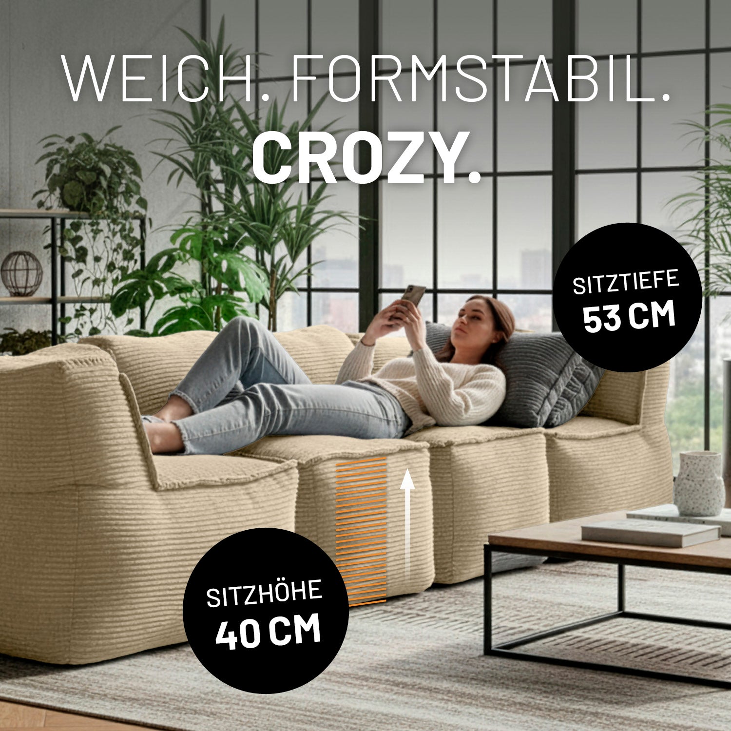 Modulare beige Lounge-Sitzlandschaft mit 40 cm Sitzhöhe und 53 cm Sitztiefe, auf der eine Frau entspannt liegend ihr Smartphone nutzt.