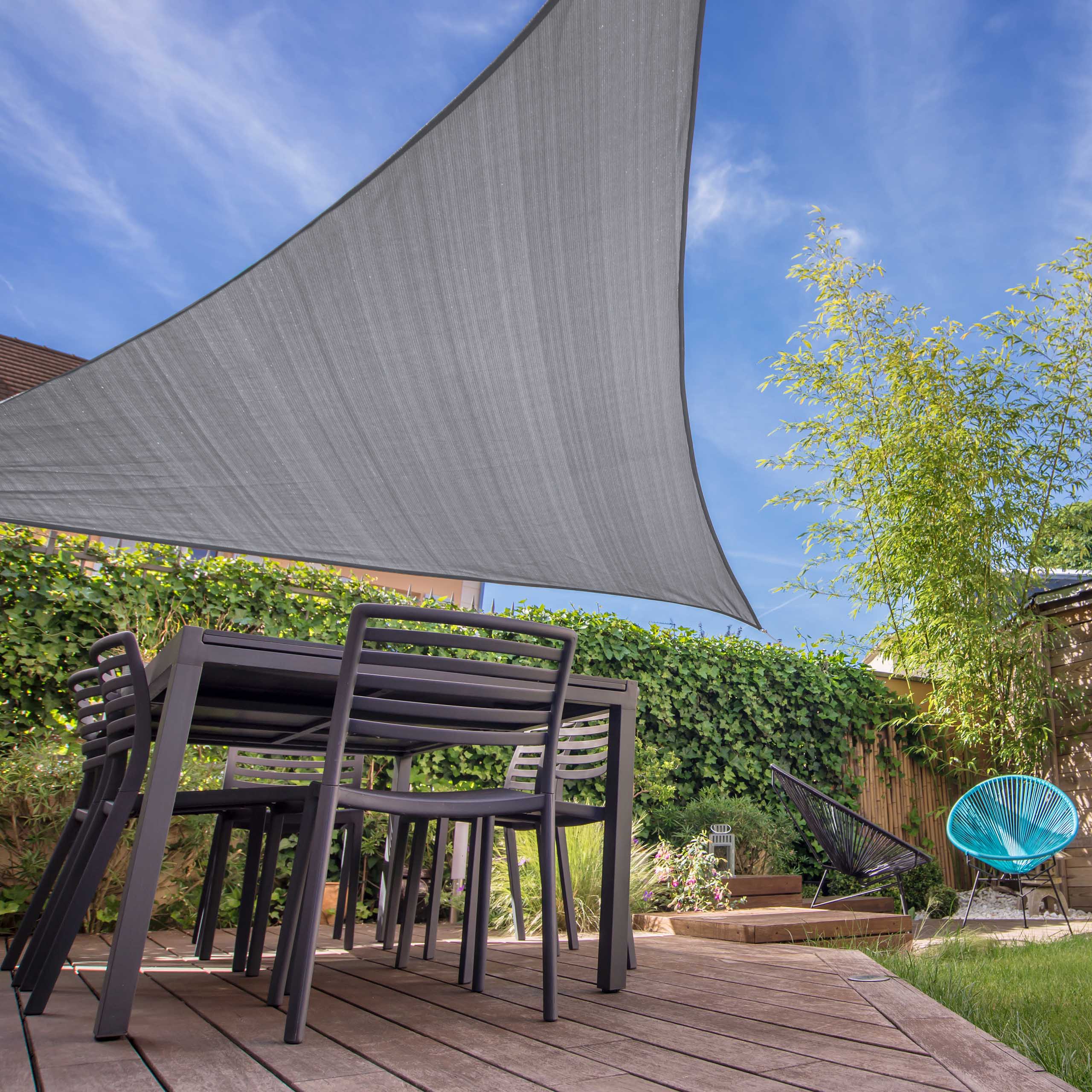 Graues Sonnensegel Dreieck über eine Terrasse in einem grünen Garten gespannt.