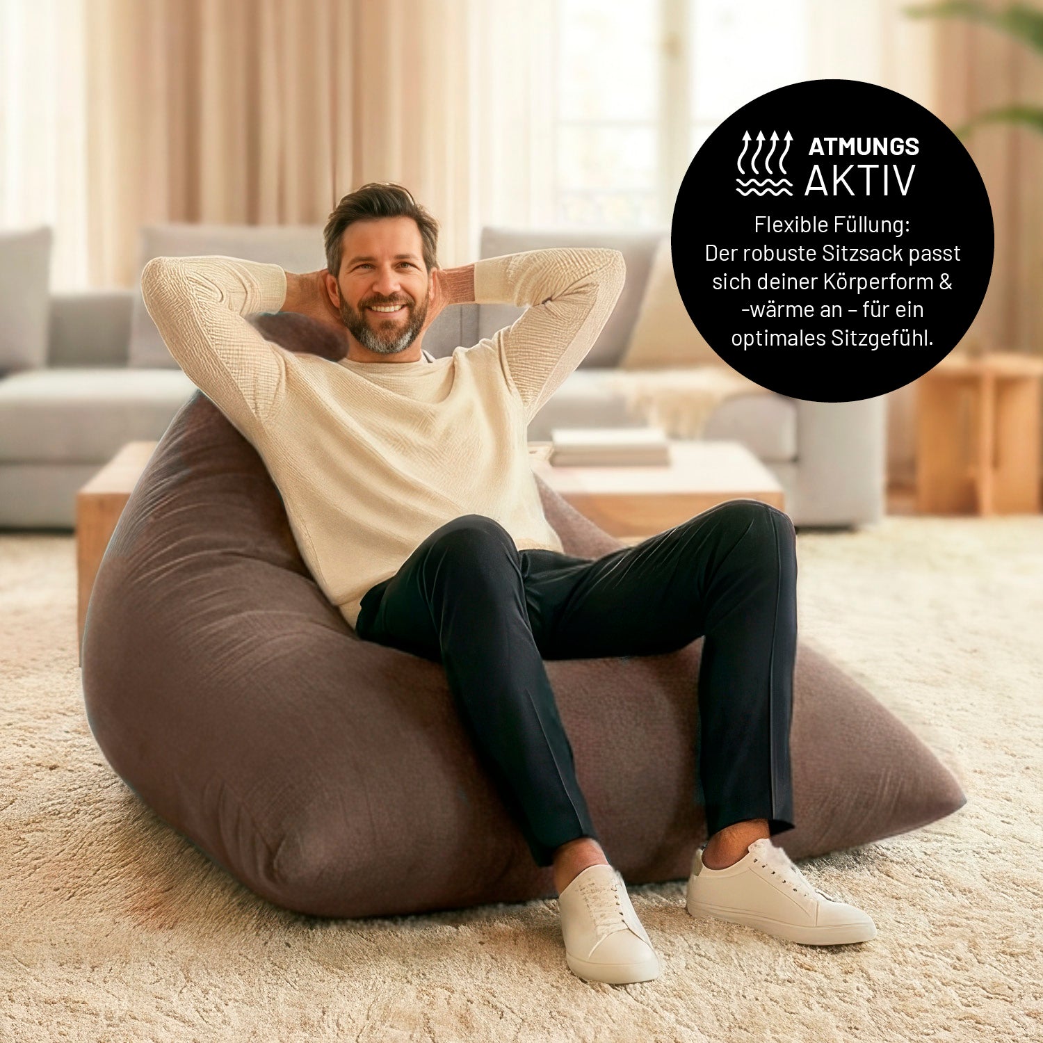 Ein Mann lehnt entspannt auf dem Sitzsack in Braun in einem Wohnzimmer. Icon zu „atmungsaktiv“ und "flexible Füllung, die sich der Körperform und Wärme anpasst".