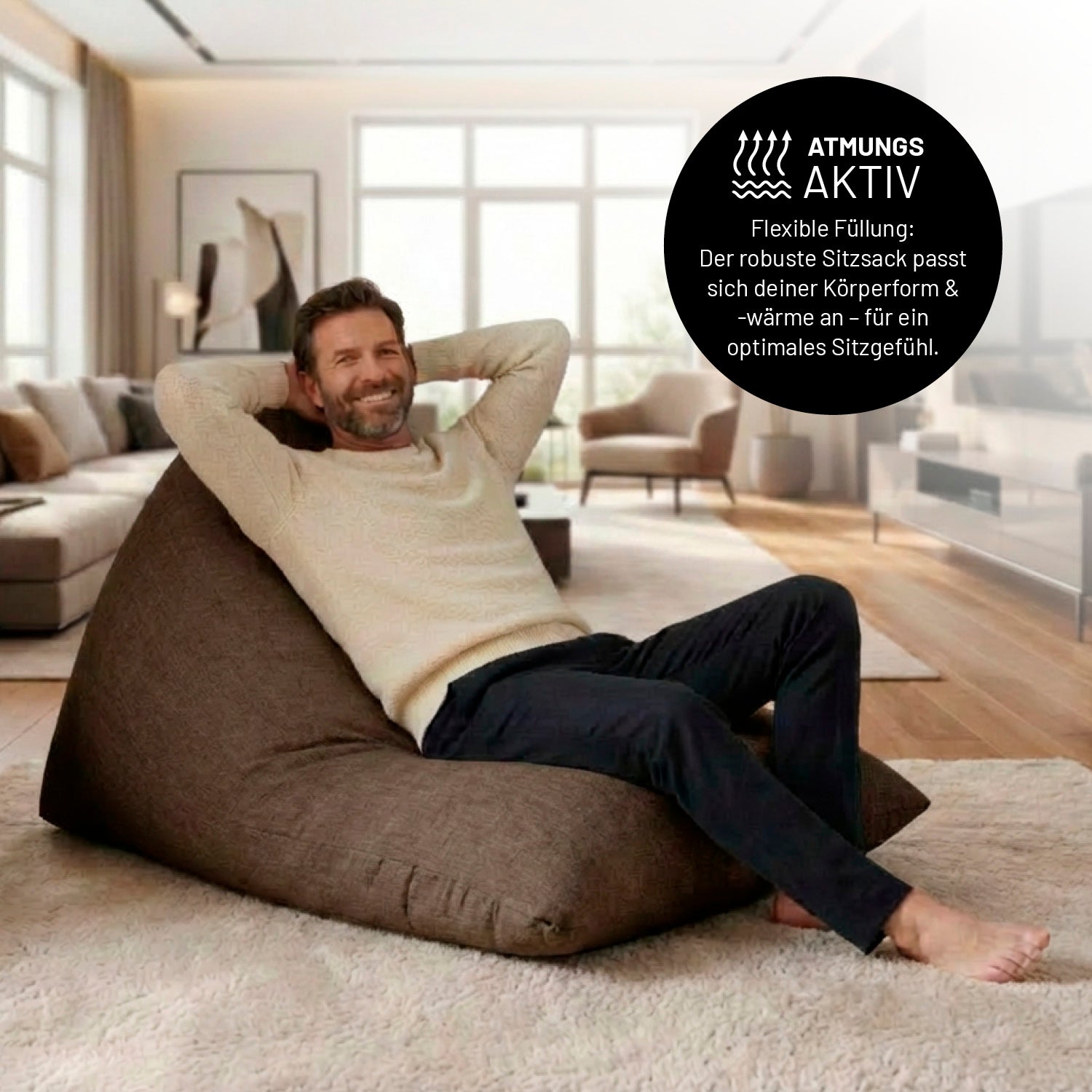 Ein Mann lehnt entspannt auf dem Sitzsack in Dunkelgrau in einem Wohnzimmer. Icon zu „atmungsaktiv“ und "flexible Füllung, die sich der Körperform und Wärme anpasst".