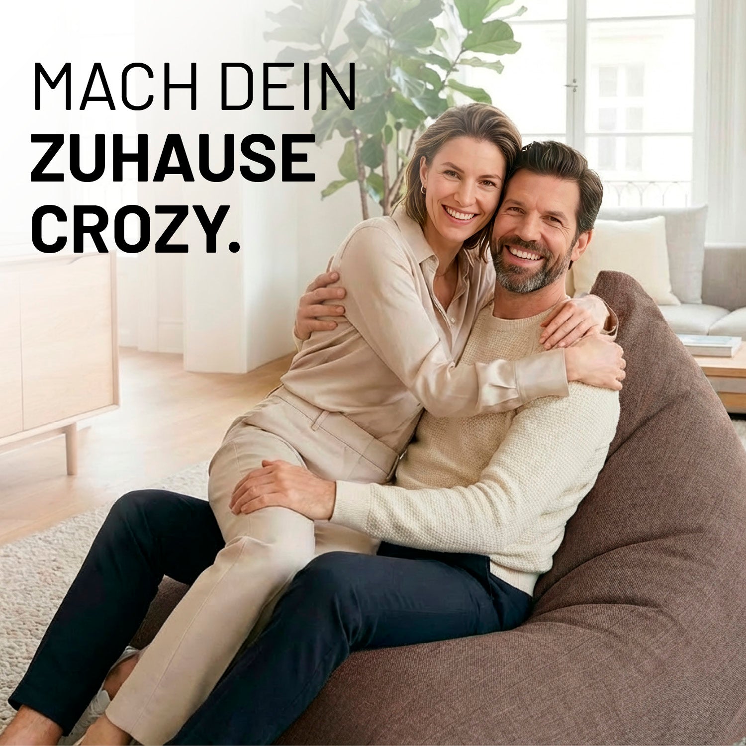 Ein lachendes Paar umarmt sich auf dem Interior Line Sitzsack in Braun im hellen Wohnzimmer; Schriftzug „Mach dein Zuhause crozy.“