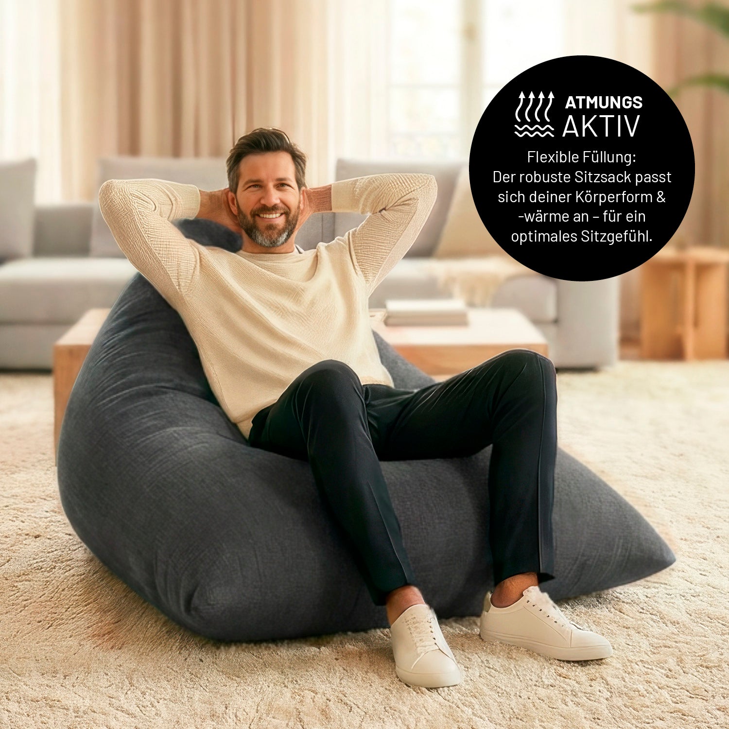 Ein Mann lehnt entspannt auf dem Sitzsack in Dunkelgrau in einem Wohnzimmer. Icon zu „atmungsaktiv“ und "flexible Füllung, die sich der Körperform und Wärme anpasst".