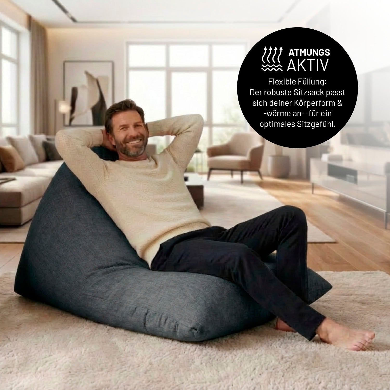 Ein Mann lehnt entspannt auf dem Sitzsack in Dunkelgrau in einem Wohnzimmer. Icon zu „atmungsaktiv“ und "flexible Füllung, die sich der Körperform und Wärme anpasst".