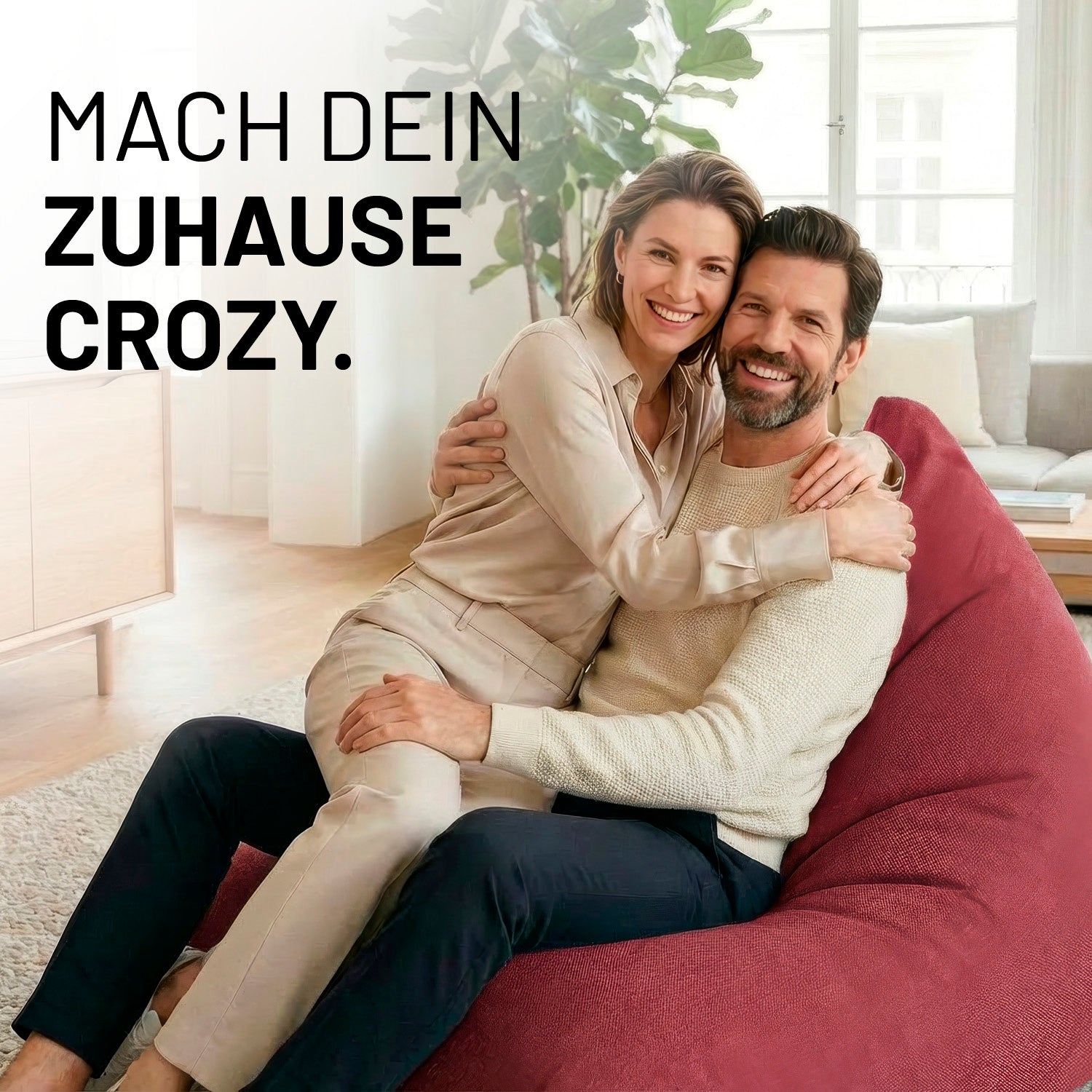 Ein lachendes Paar umarmt sich auf dem Interior Line Sitzsack in Rot im hellen Wohnzimmer; Schriftzug „Mach dein Zuhause crozy.“