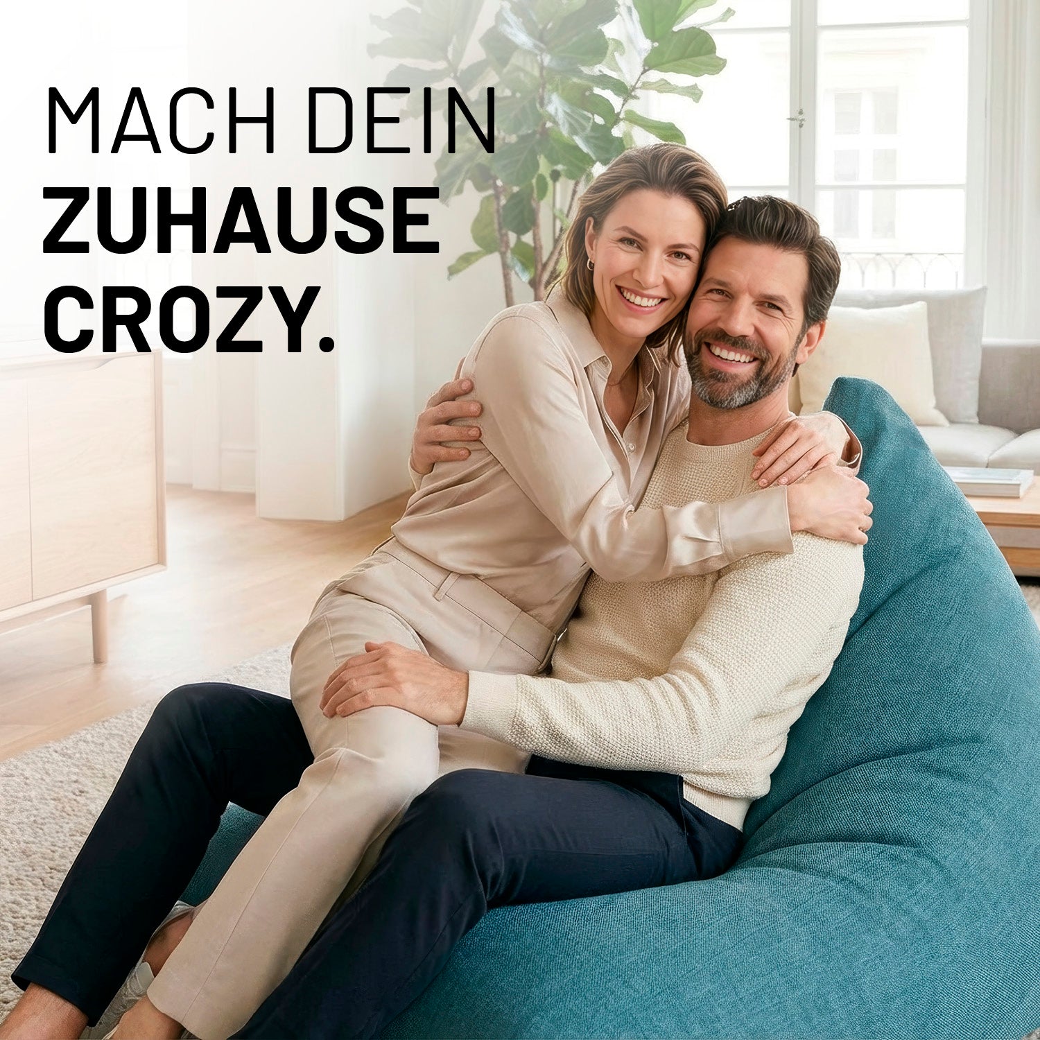 Ein lachendes Paar umarmt sich auf dem Interior Line Sitzsack in Aquamarin im hellen Wohnzimmer; Schriftzug „Mach dein Zuhause crozy.“