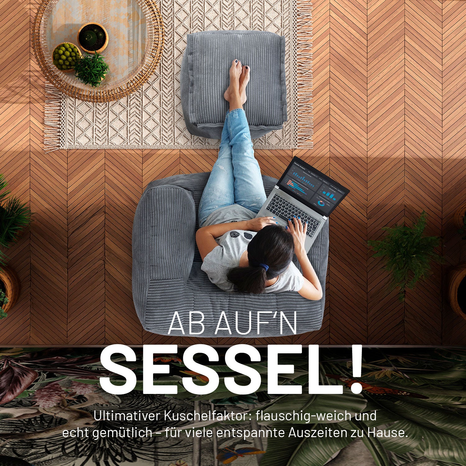 Frau mit Laptop sitzt auf dem grauen modularen Sitzsack-Sessel in Cord und hat die Füße auf dem passenden Cord-Pouf/Hocker.