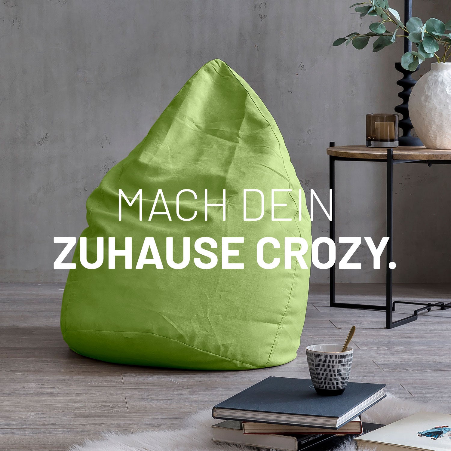 Großer Sitzsack in Grün in modernem Wohnambiente mit Tisch, Büchern und Tasse. Text: "Mach dein Zuhause crozy."