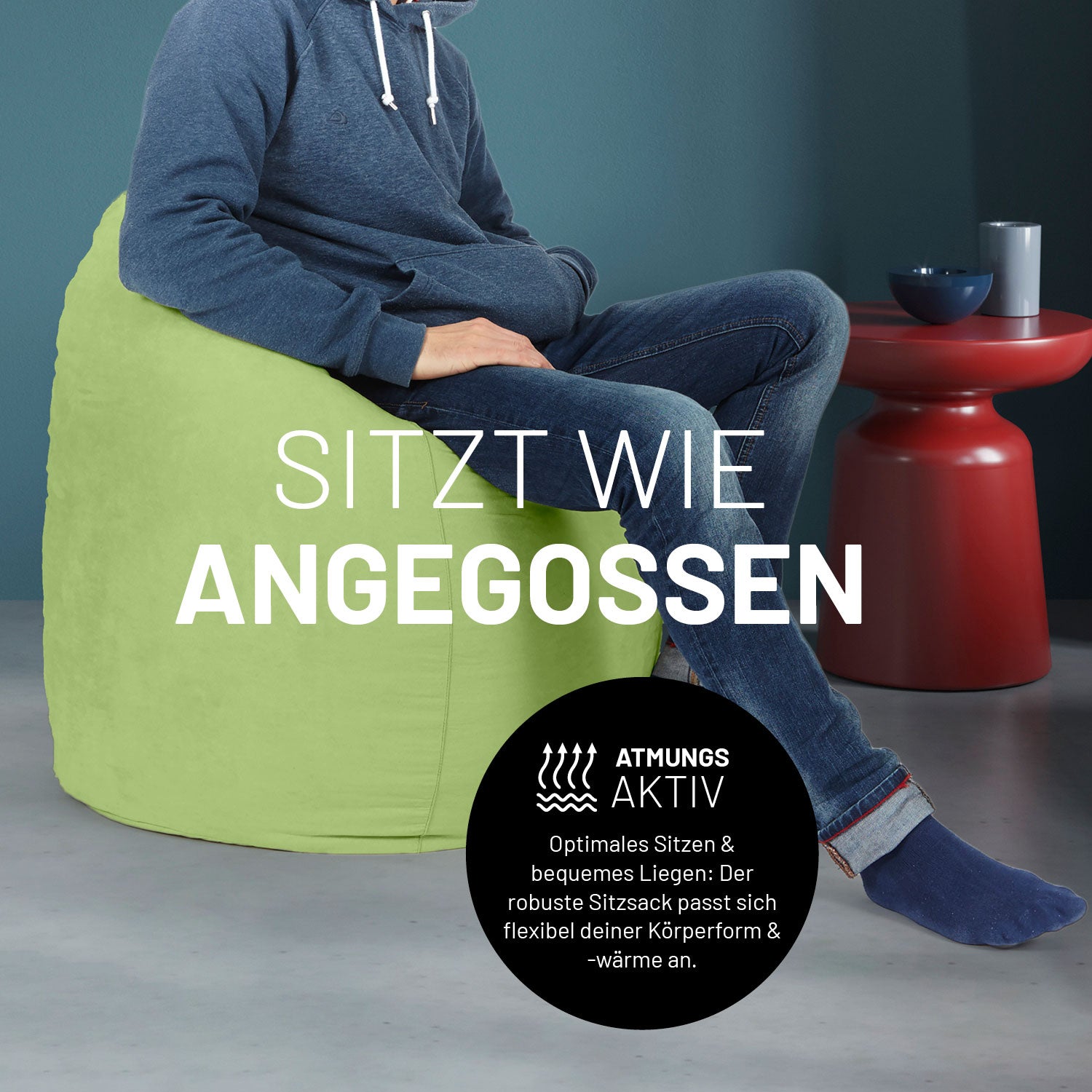 Ein Mann sitzt im grünen Sitzsack, dahinter ein roter Tisch. Icon "Atmungsaktiv - Passt sich der Körperform und -wärme an".
