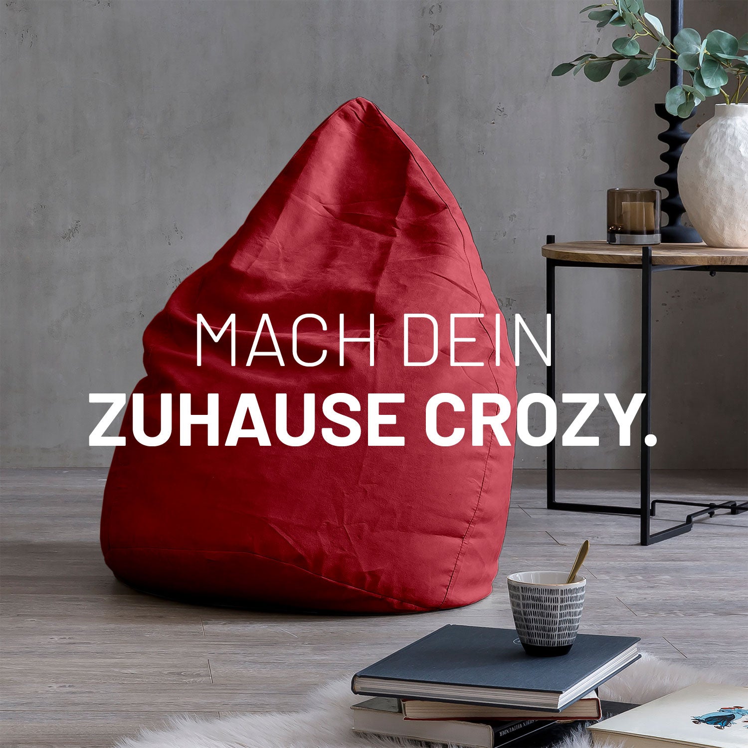 Großer Sitzsack in Rot in modernem Wohnambiente mit Tisch, Büchern und Tasse. Text: "Mach dein Zuhause crozy."