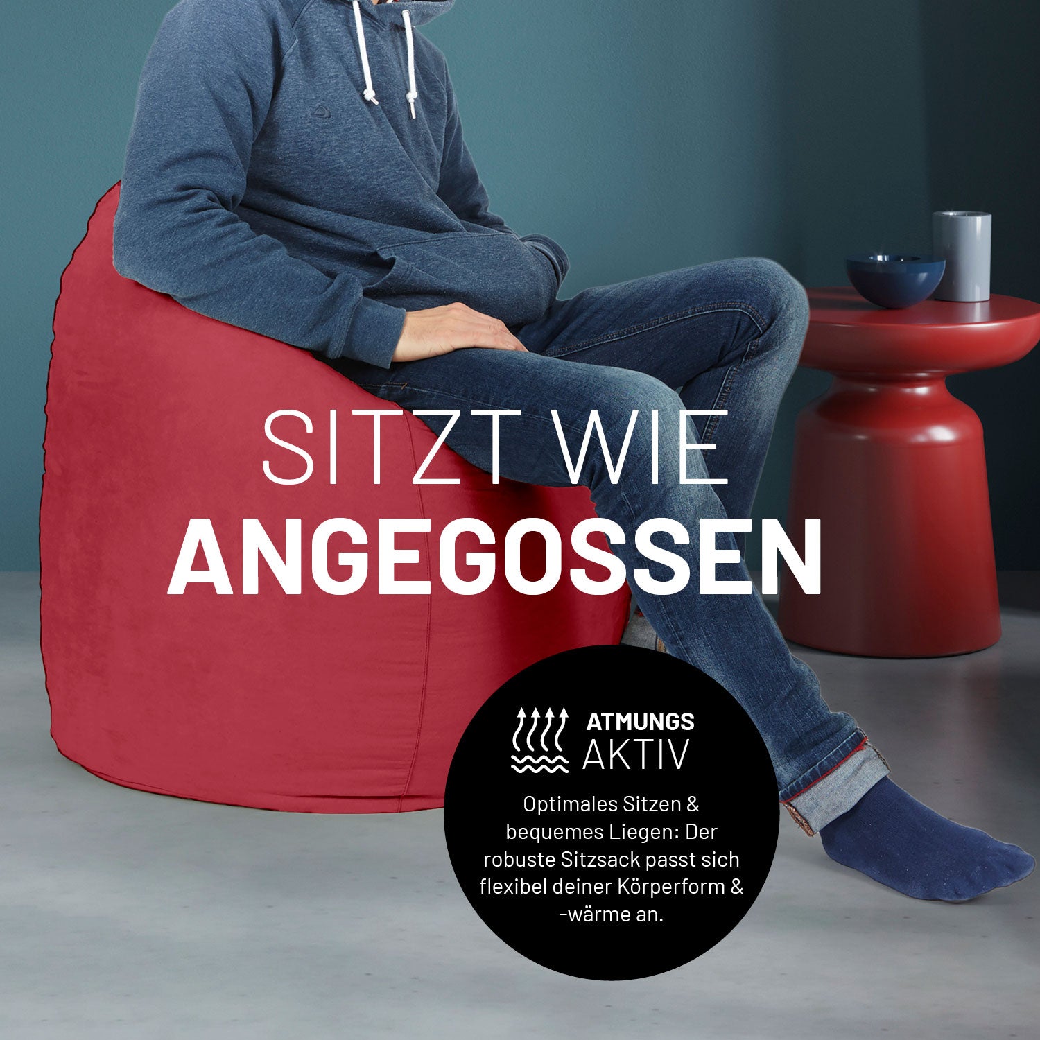 Ein Mann sitzt im roten Sitzsack, dahinter ein roter Tisch. Icon "Atmungsaktiv - Passt sich der Körperform und -wärme an".