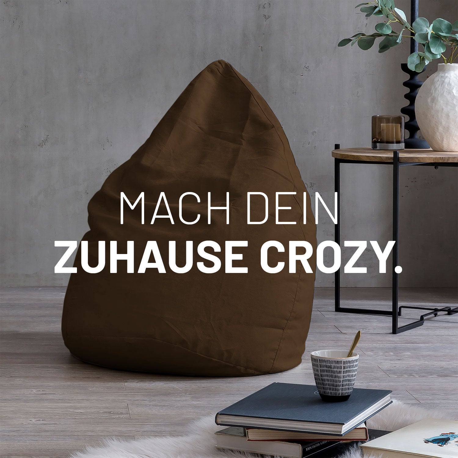 Großer Sitzsack in Braun in modernem Wohnambiente mit Tisch, Büchern und Tasse. Text: "Mach dein Zuhause crozy."
