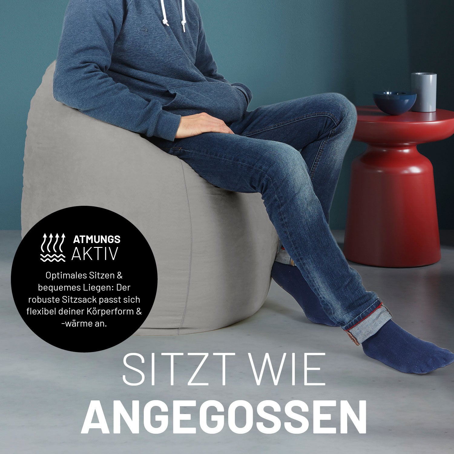 Ein Mann sitzt im grauen Sitzsack, dahinter ein roter Tisch. Icon "Atmungsaktiv - Passt sich der Körperform und -wärme an".