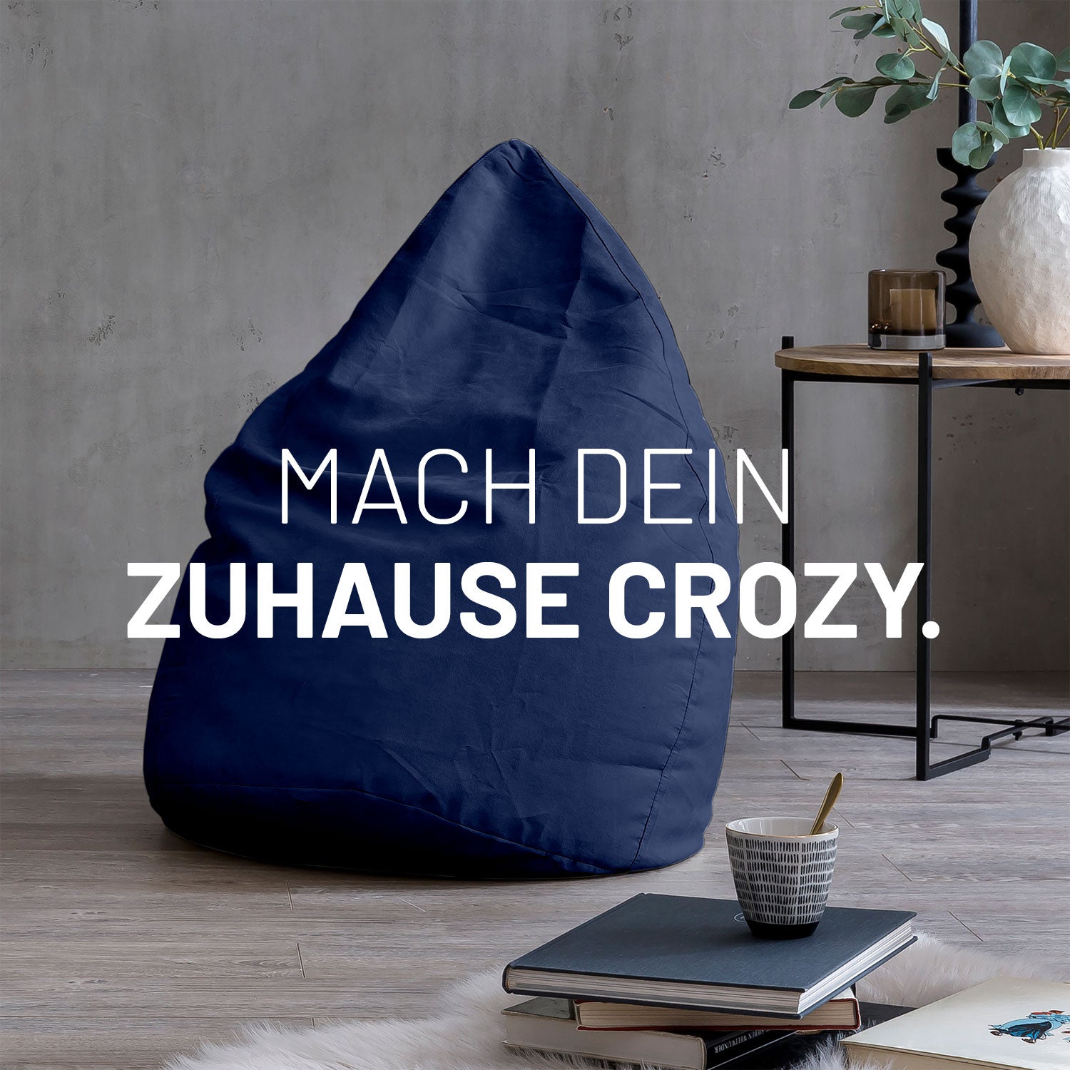 Großer Sitzsack in Navy in modernem Wohnambiente mit Tisch, Büchern und Tasse. Text: "Mach dein Zuhause crozy."