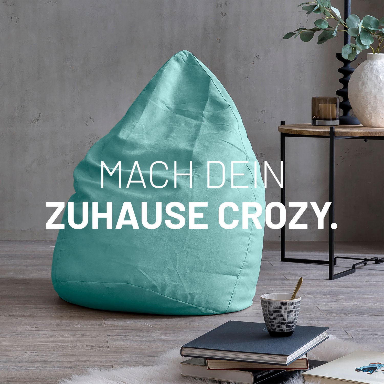 Großer Sitzsack in Türkis in modernem Wohnambiente mit Tisch, Büchern und Tasse. Text: "Mach dein Zuhause crozy."