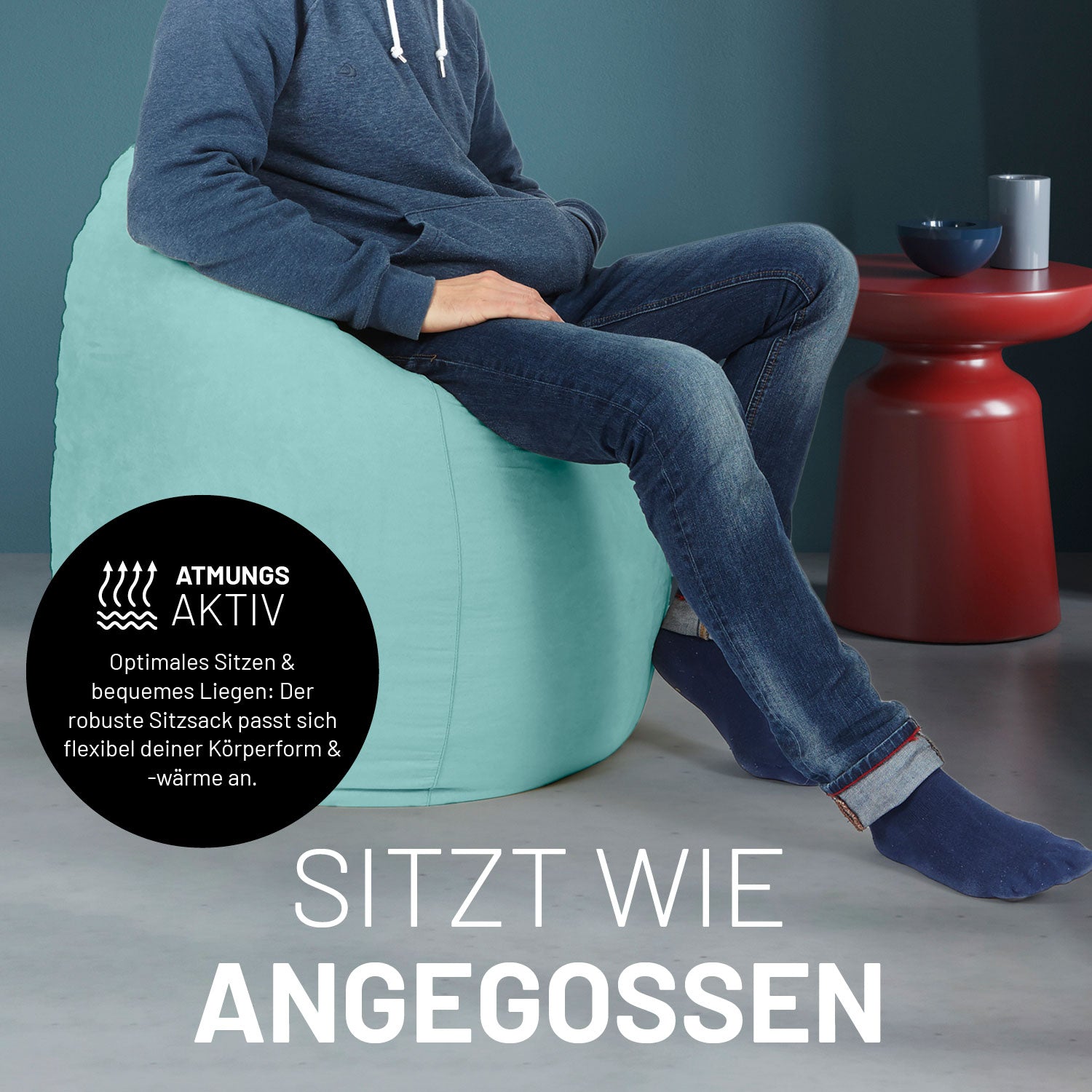 Ein Mann sitzt im türkisen Sitzsack, dahinter ein roter Tisch. Icon "Atmungsaktiv - Passt sich der Körperform und -wärme an".