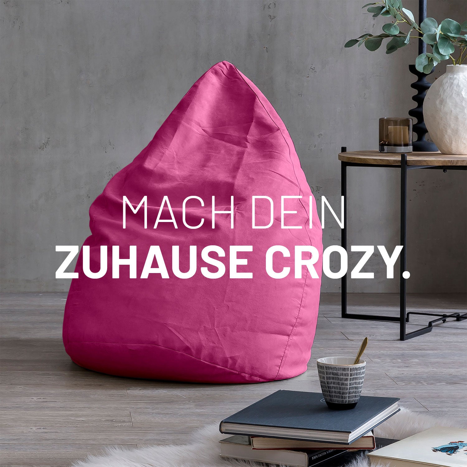 Großer Sitzsack in Pink in modernem Wohnambiente mit Tisch, Büchern und Tasse. Text: "Mach dein Zuhause crozy."