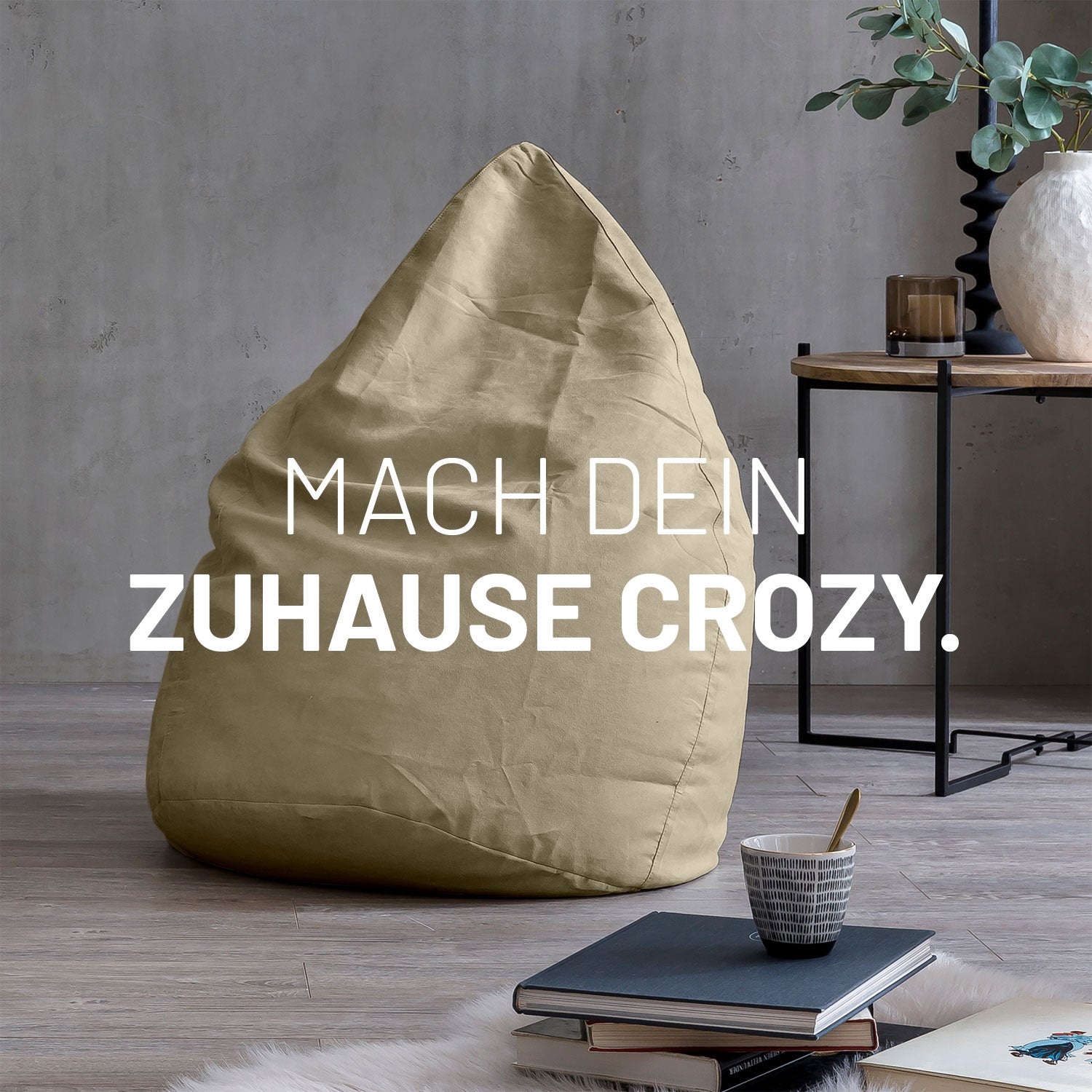 Großer Sitzsack in Beige in modernem Wohnambiente mit Tisch, Büchern und Tasse. Text: "Mach dein Zuhause crozy."