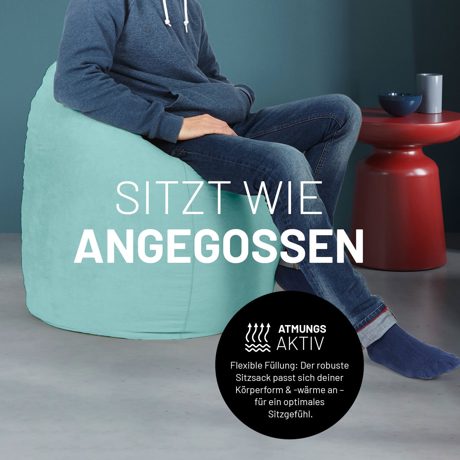 Ein Mann sitzt im türkisen Sitzsack, dahinter ein roter Tisch. Icon "Atmungsaktiv - Passt sich der Körperform und -wärme an".