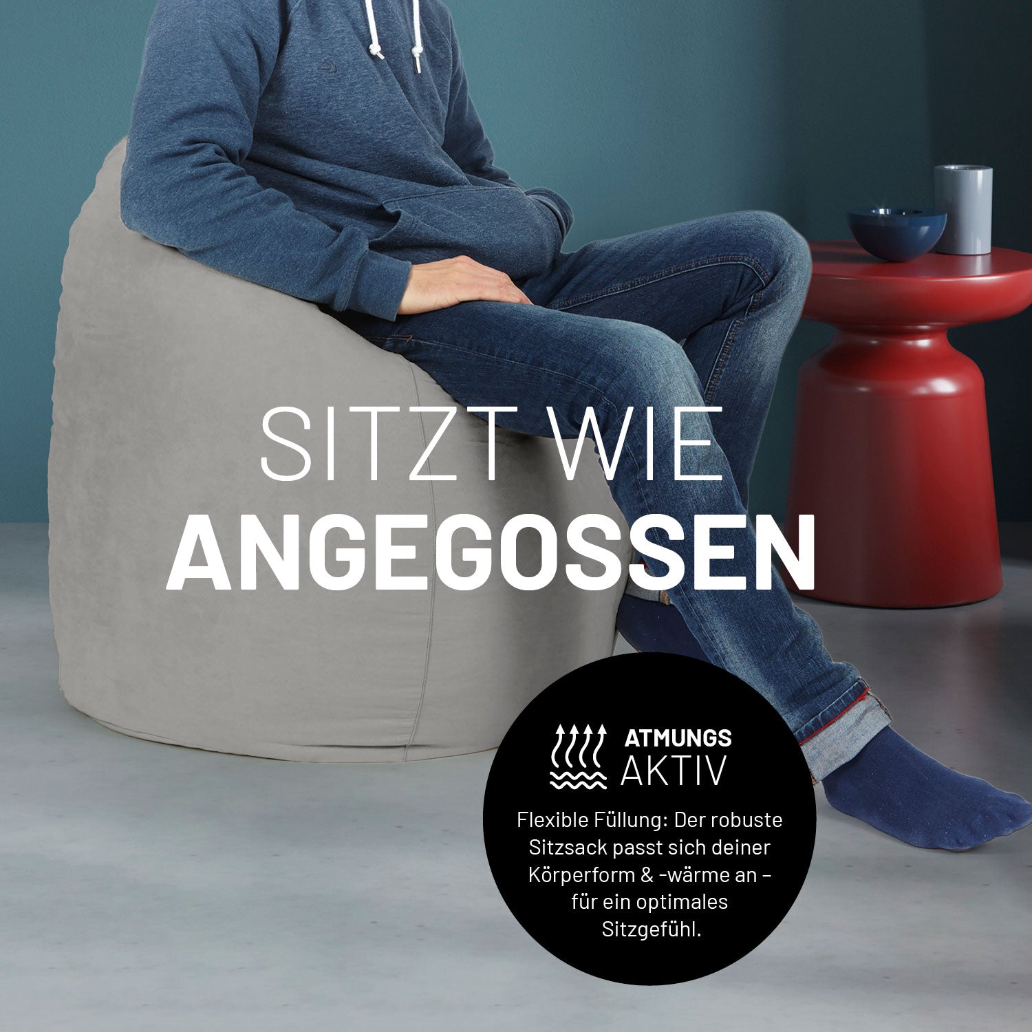Ein Mann sitzt im grauen Sitzsack, dahinter ein roter Tisch. Icon "Atmungsaktiv - Passt sich der Körperform und -wärme an".
