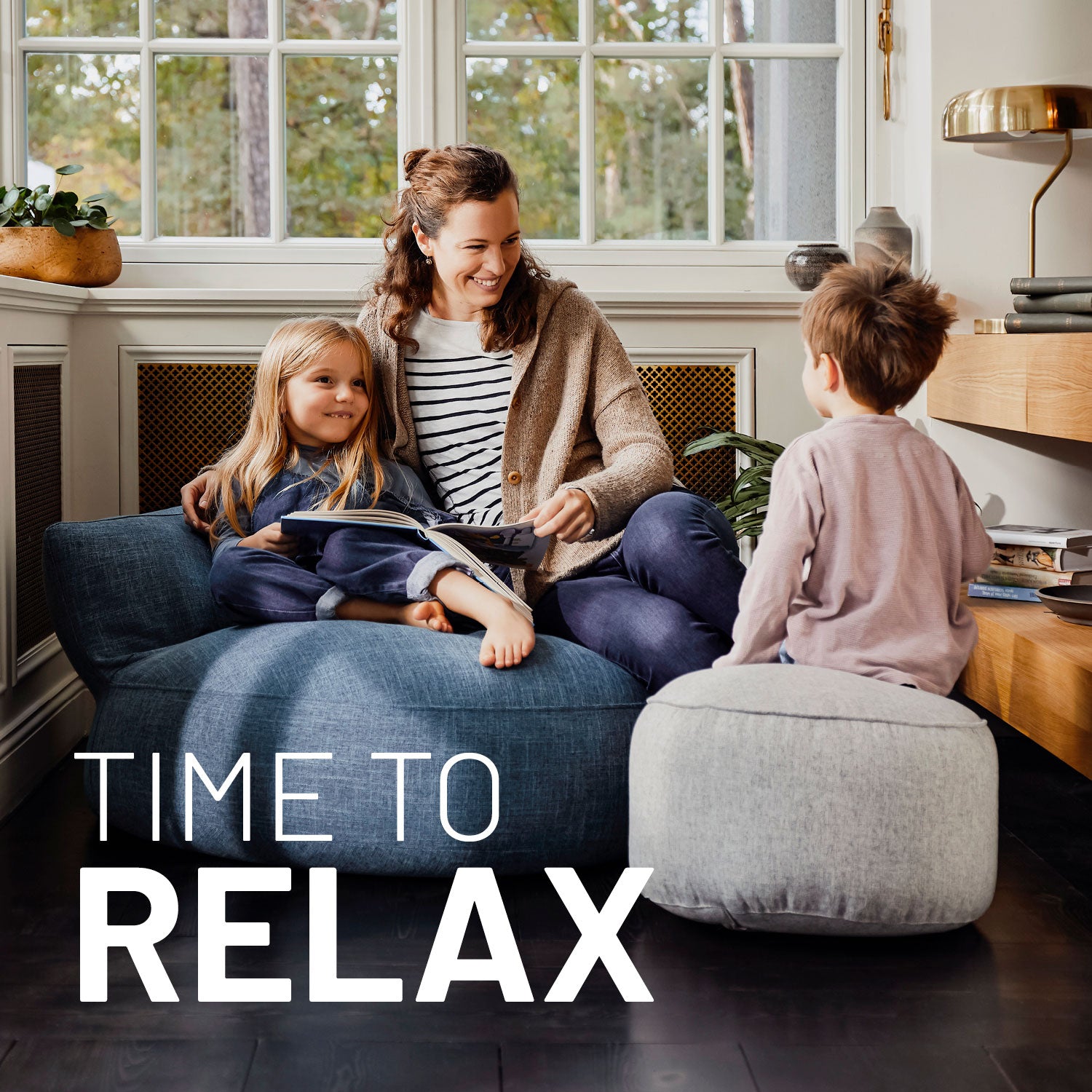 Eine Frau mit zwei Kindern sitzt in einer gemütlichen Leseecke auf dem Sitzsack-Sofa und dem Pouf aus der Comfort Line, Text "Time to Relax".