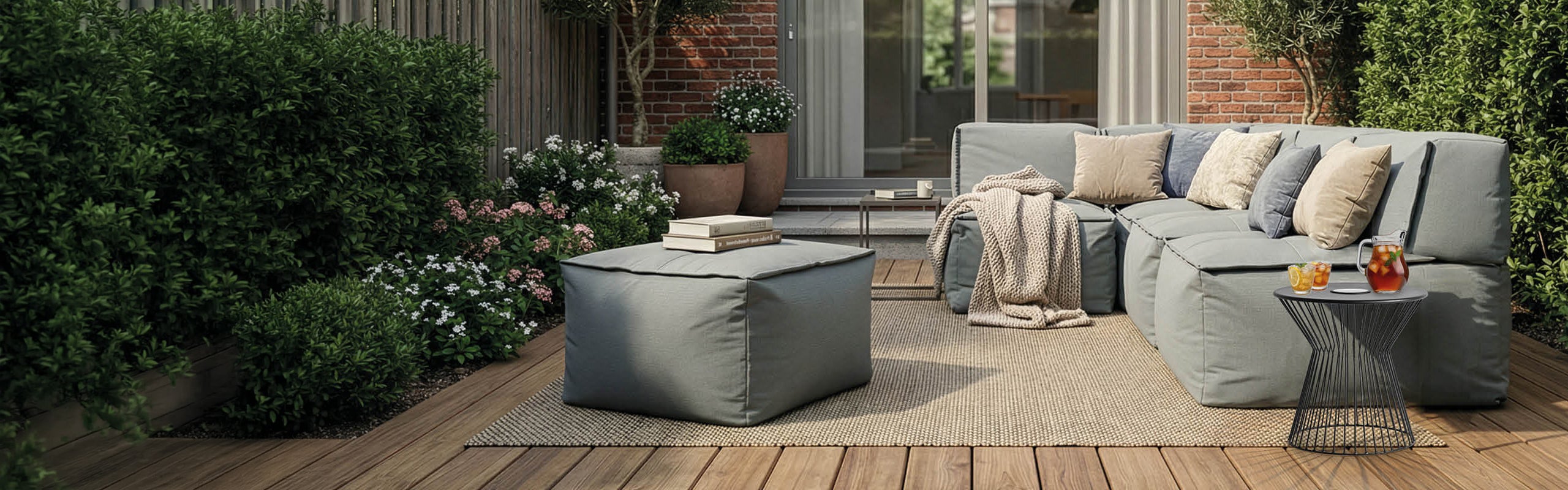 Modernes Outdoor-Wohnzimmer mit modularem Loungesofa und Hocker auf der Terrasse, ergänzt durch Kissen, Decke und sommerliche Deko.