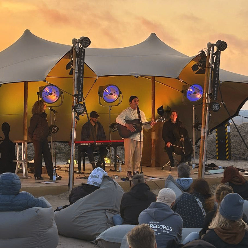 Konzert am Strand mit Personen die auf den grauen LUMALAND Sitzsäcken sitzen.