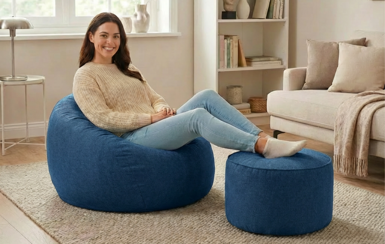 Eine Frau sitzt entspannt im LUMALAND Comfort Line Sitzsack mit passendem Hocker im gemütlichen Wohnzimmer.