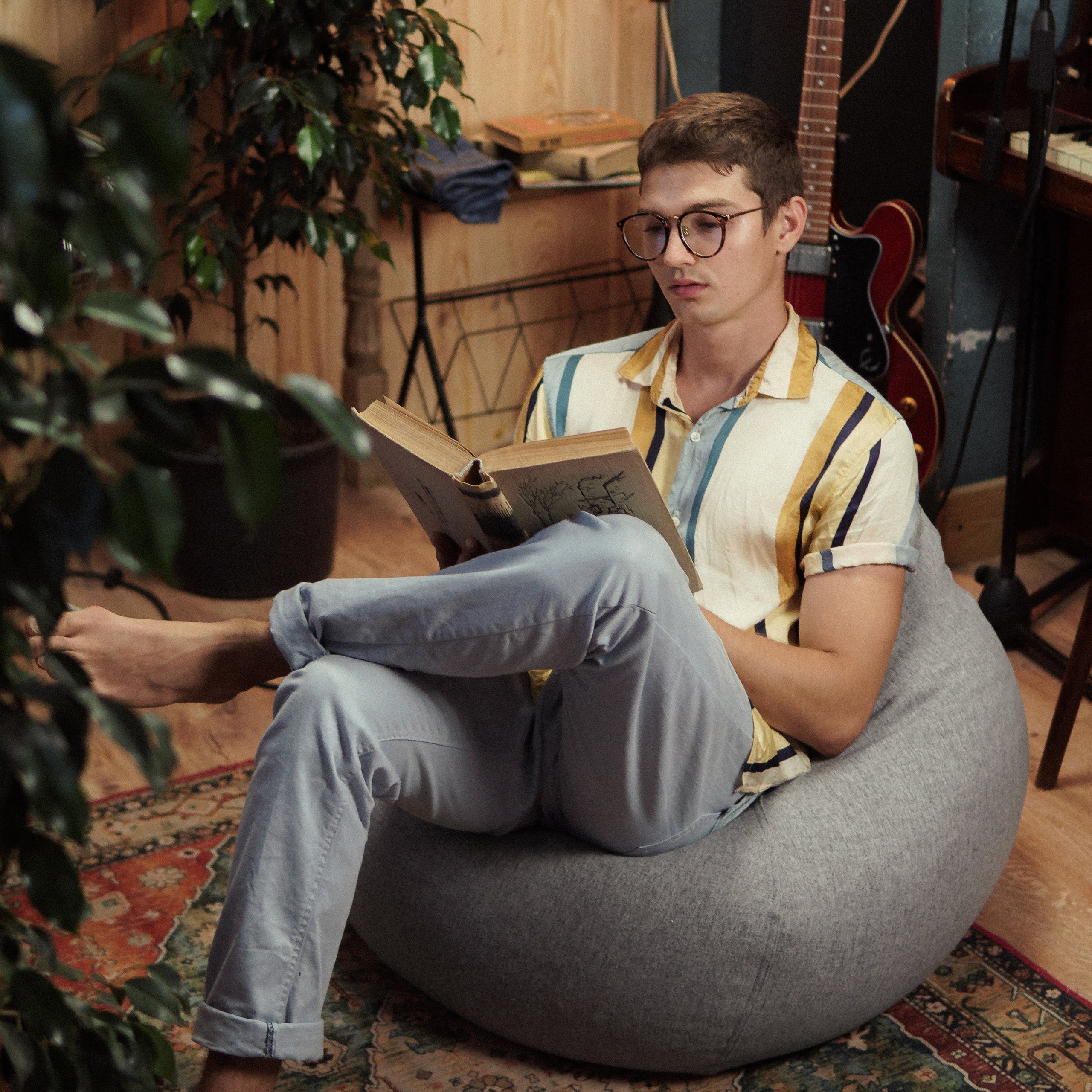 Ein Mann sitzt im Comfort Line Sitzsack in Hellgrau, hat die Beine überschlagen und ließt ein Buch.