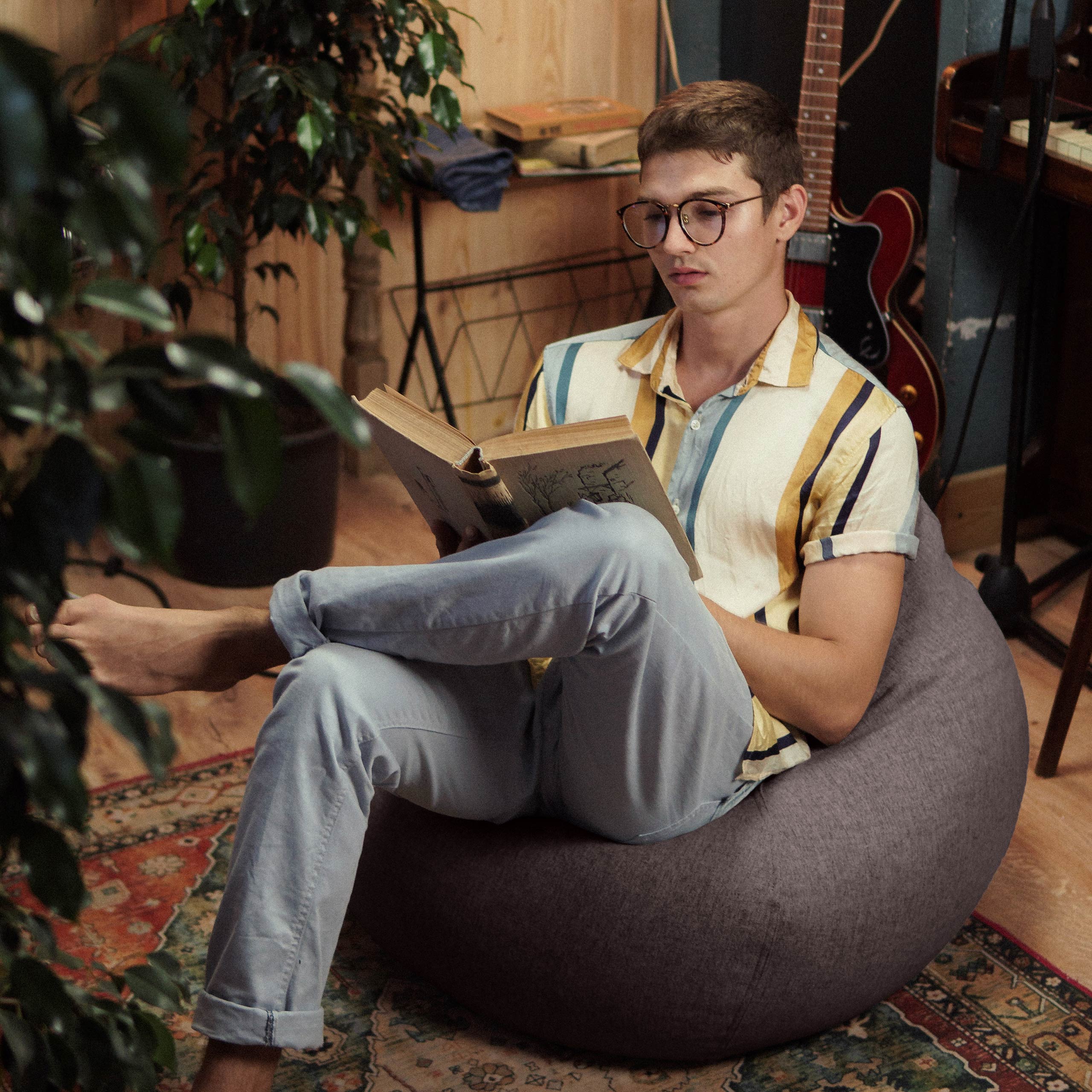 Ein Mann sitzt im Comfort Line Sitzsack in Dunkelgrau, hat die Beine überschlagen und ließt ein Buch.