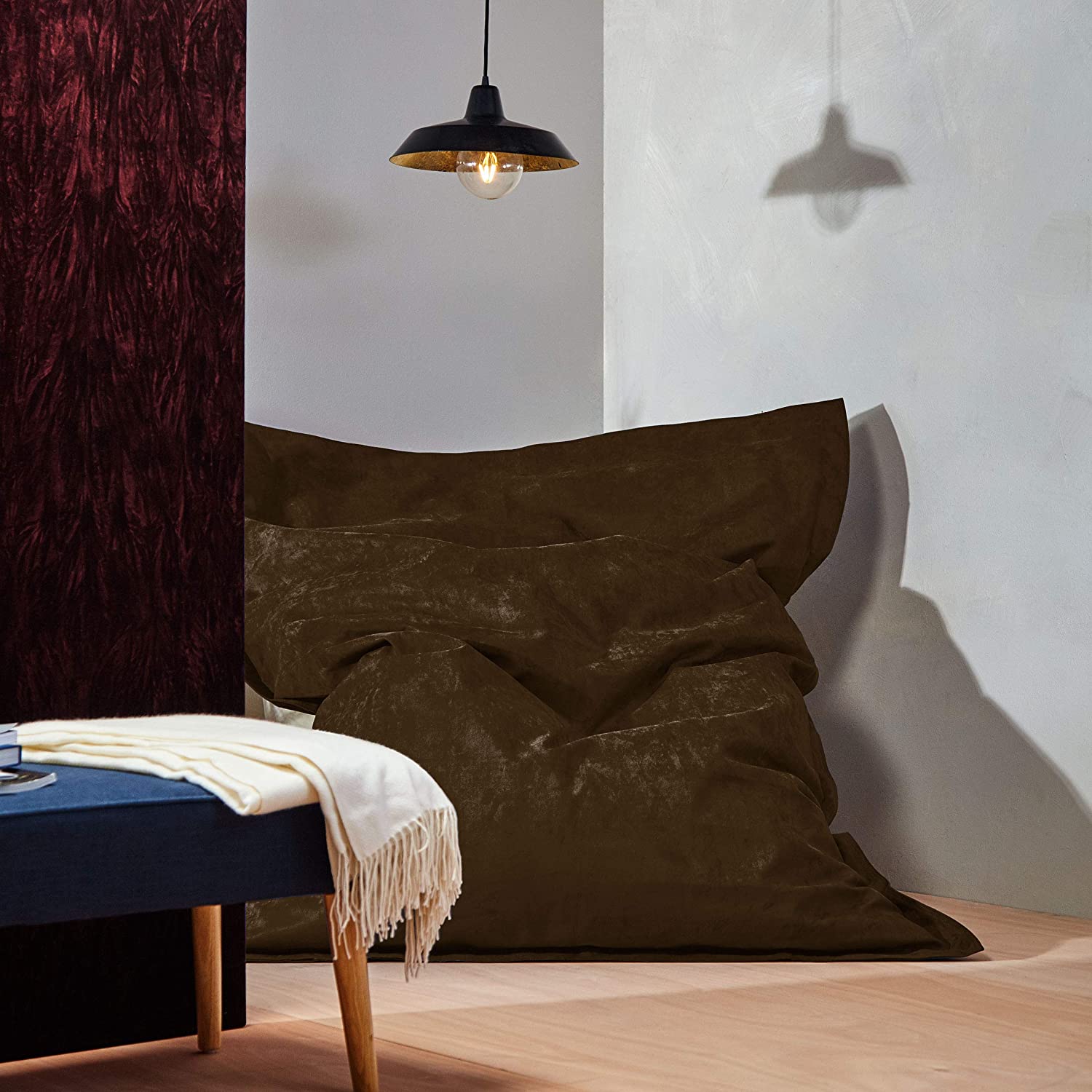 Der XXL Microvelours Sitzsack in Braun liegt in der Ecke eines Wohnzimmer, oben drüber eine Lampe, davor ein Tisch.