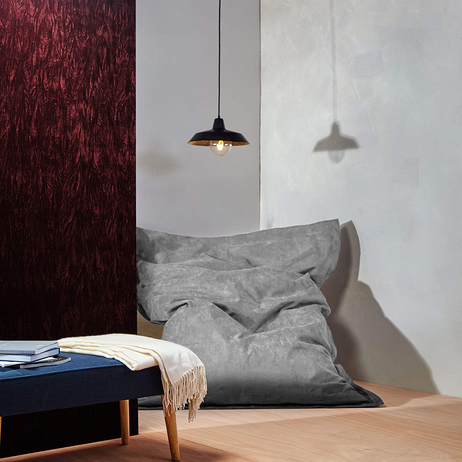 Der XXL Microvelours Sitzsack in Grau liegt in der Ecke eines Wohnzimmer, oben drüber eine Lampe, davor ein Tisch.