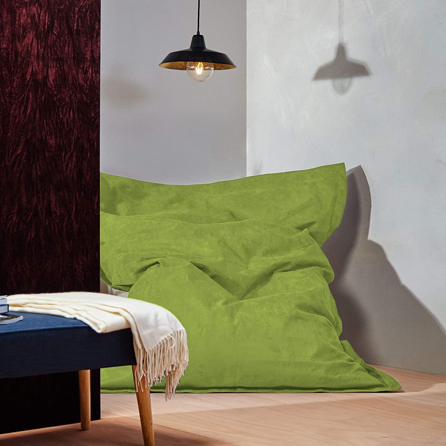 Der XXL Microvelours Sitzsack in Grün liegt in der Ecke eines Wohnzimmer, oben drüber eine Lampe, davor ein Tisch.