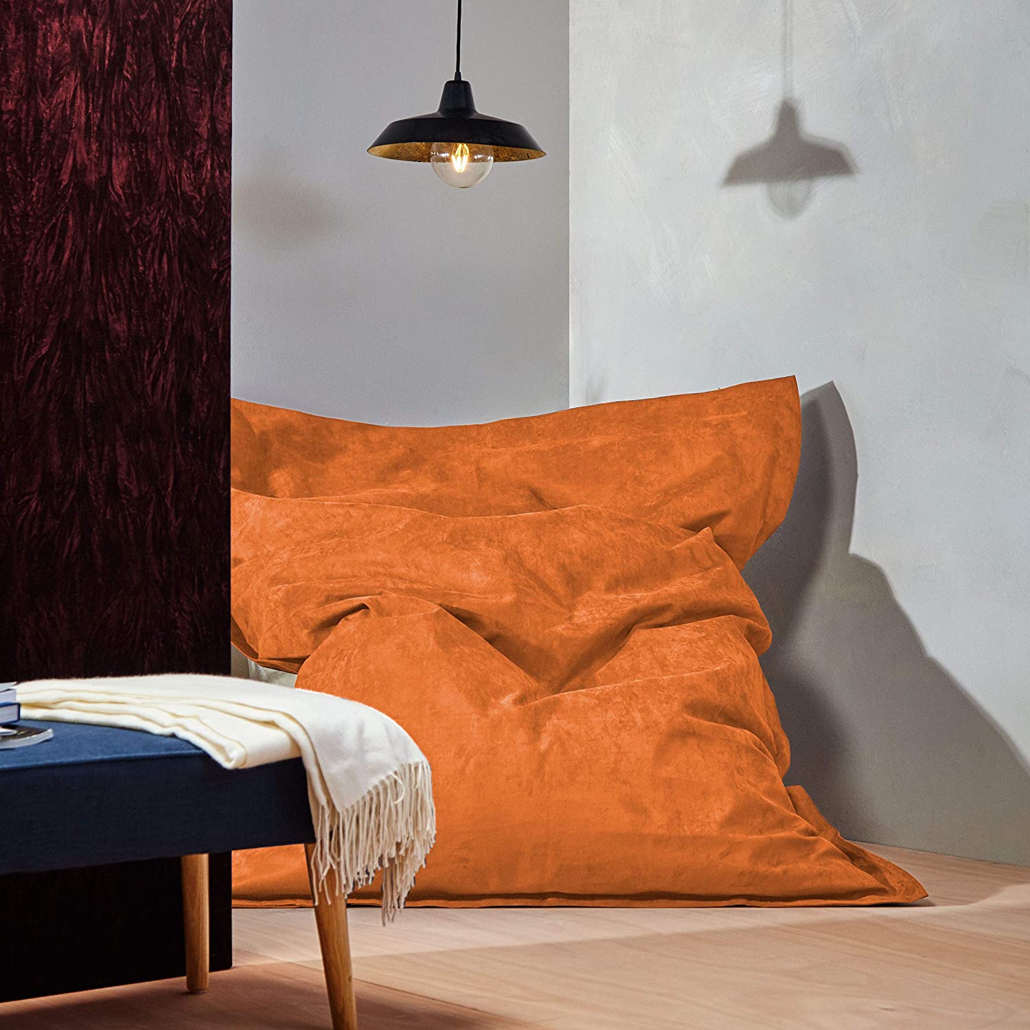 Der XXL Microvelours Sitzsack in Orange liegt in der Ecke eines Wohnzimmer, oben drüber eine Lampe, davor ein Tisch.