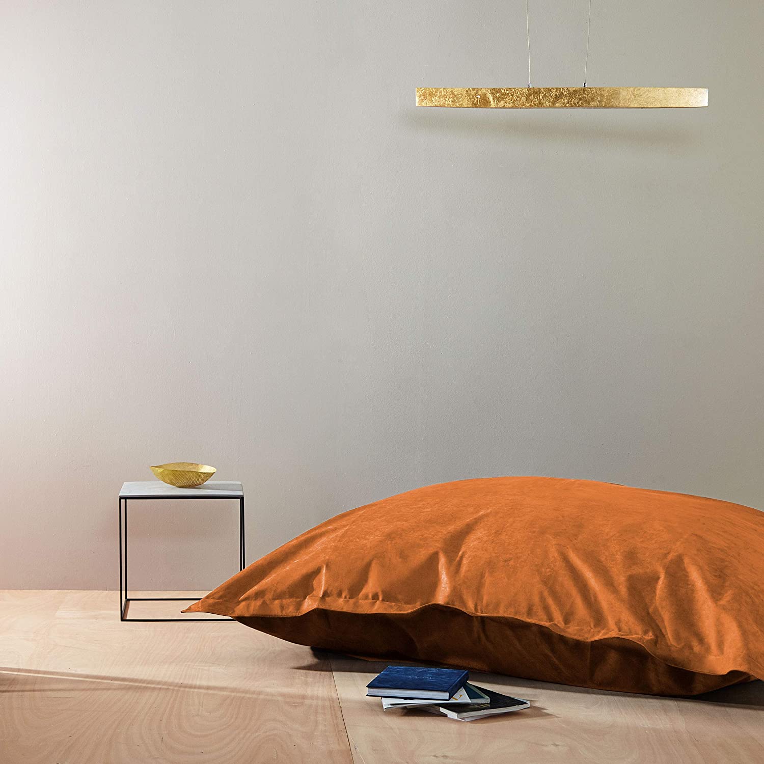 Der orange XXL Microvelours Sitzsack liegt in einem spartanisch eingerichteten Raum als Sitzkissen auf dem Boden.