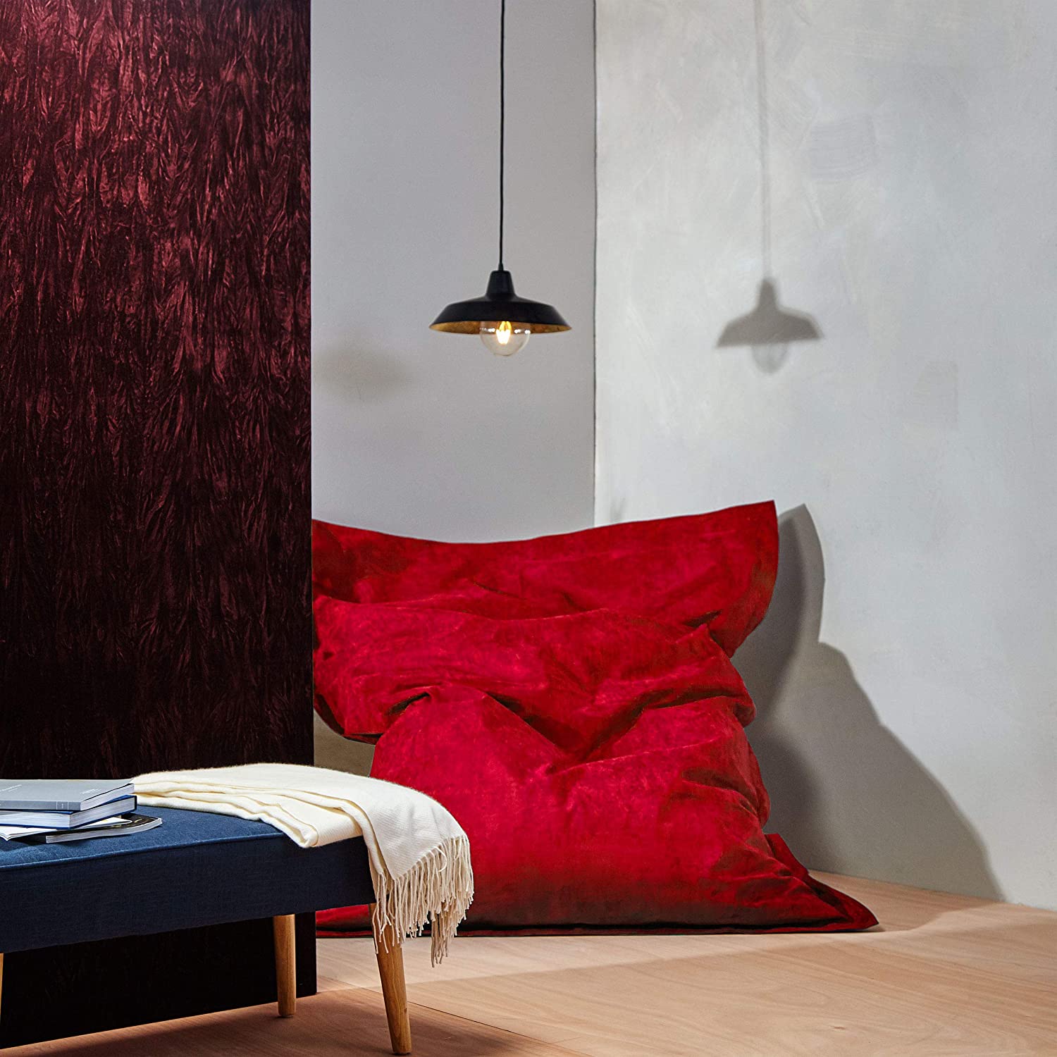Der XXL Microvelours Sitzsack in Rot liegt in der Ecke eines Wohnzimmer, oben drüber eine Lampe, davor ein Tisch.