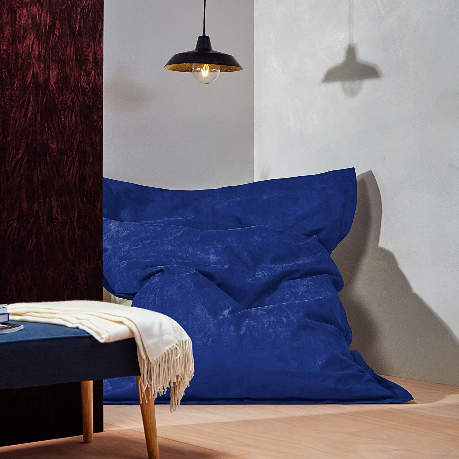 Der XXL Microvelours Sitzsack in Royalblau liegt in der Ecke eines Wohnzimmer, oben drüber eine Lampe, davor ein Tisch.