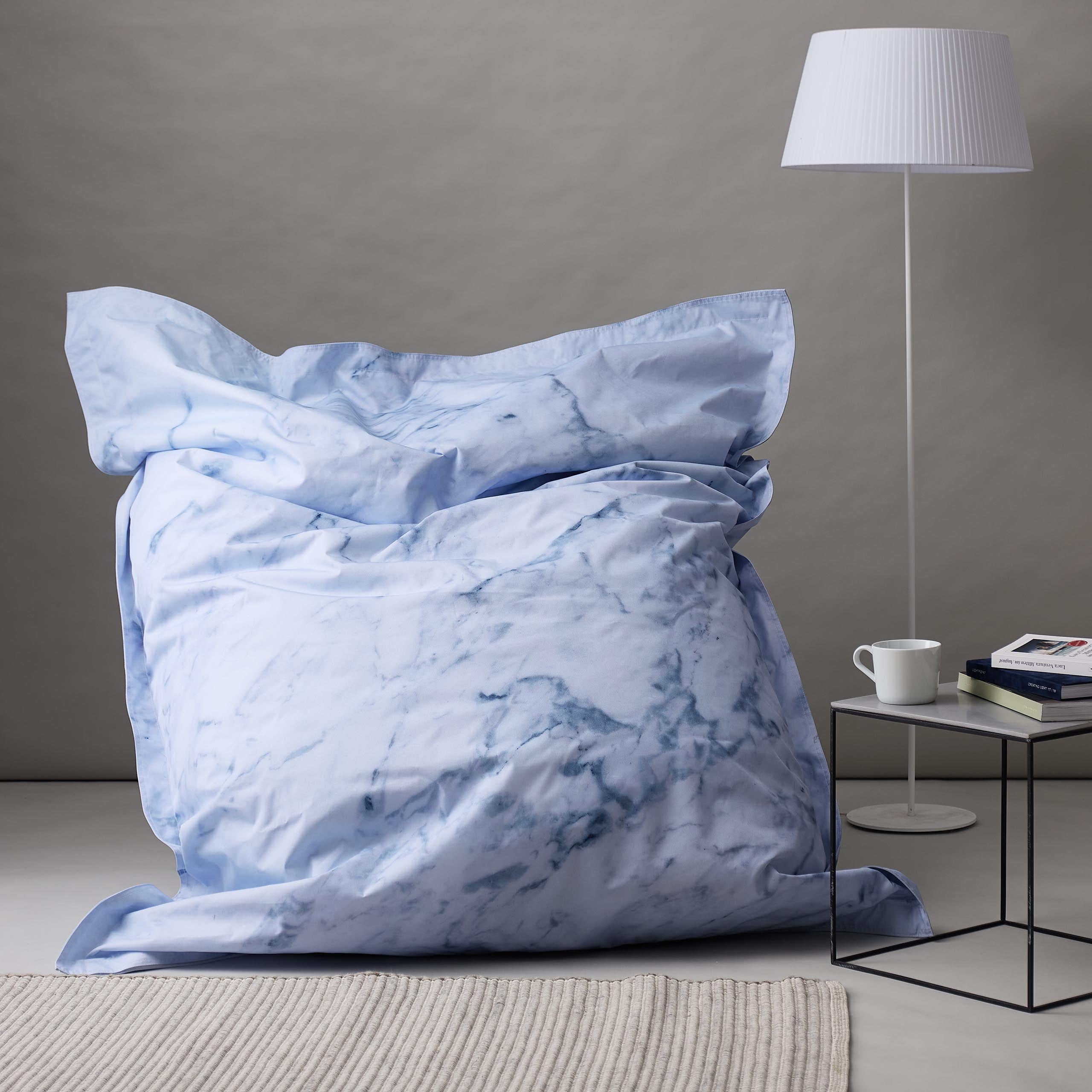 LUMALAND XXL Sitzsack Printed Edition in Marmor-Optik in einem Wohnzimmer, daneben eine Stehlampe und ein Tisch.