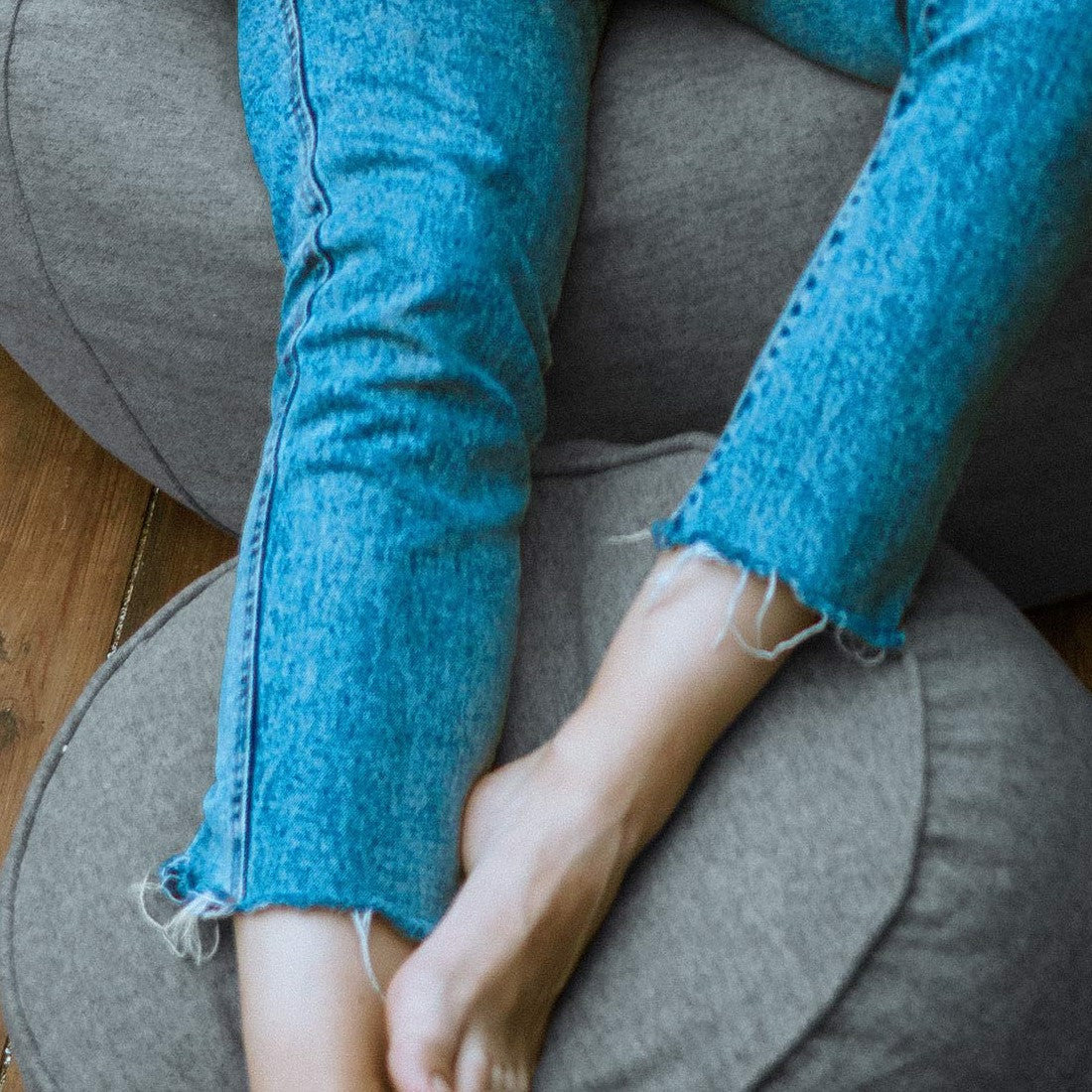Auf dem hellgrauen Hocker/Pouf aus der Comfort Line abgelegte Beine einer Frau - Verwendung als Fußschemel.