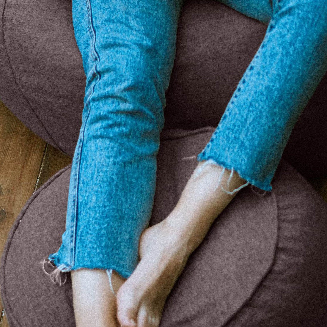 Auf dem dunkelgrauen Hocker/Pouf aus der Comfort Line abgelegte Beine einer Frau - Verwendung als Fußschemel.