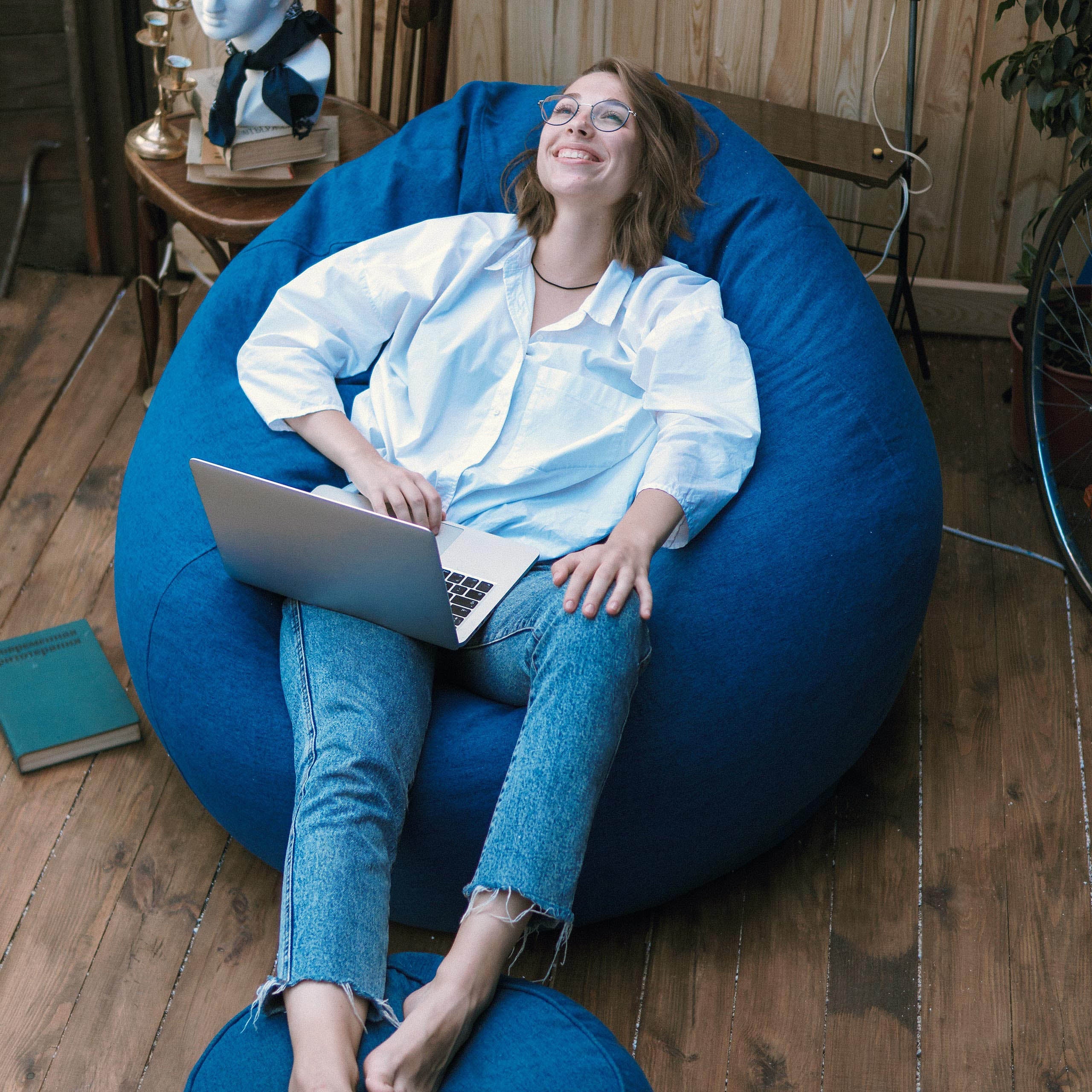 Eine Frau sitzt im Comfort Line Sitzsack in Navy, vor ihr ein Laptop und hat ihre Füße auf dem Hocker abgestellt.
