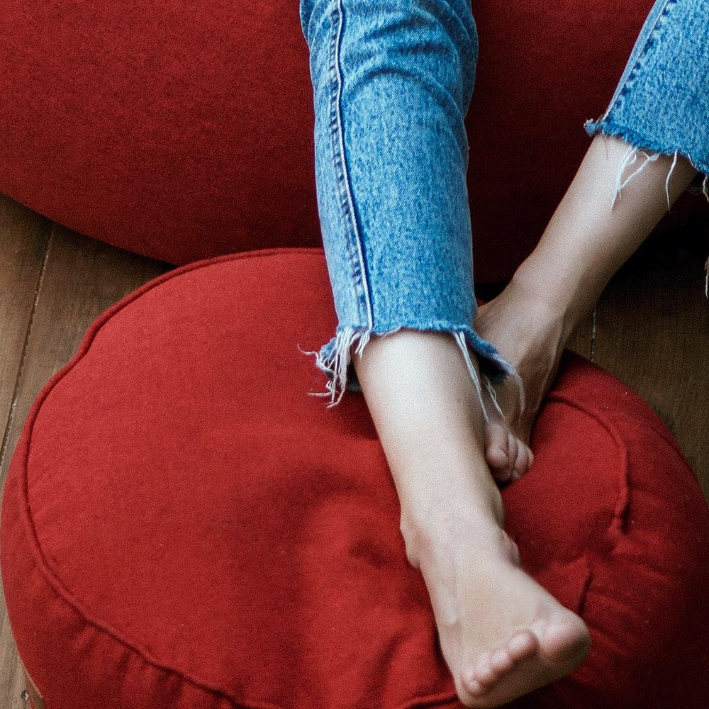 Auf dem roten Hocker/Pouf aus der Comfort Line abgelegte Beine einer Frau - Verwendung als Fußschemel.