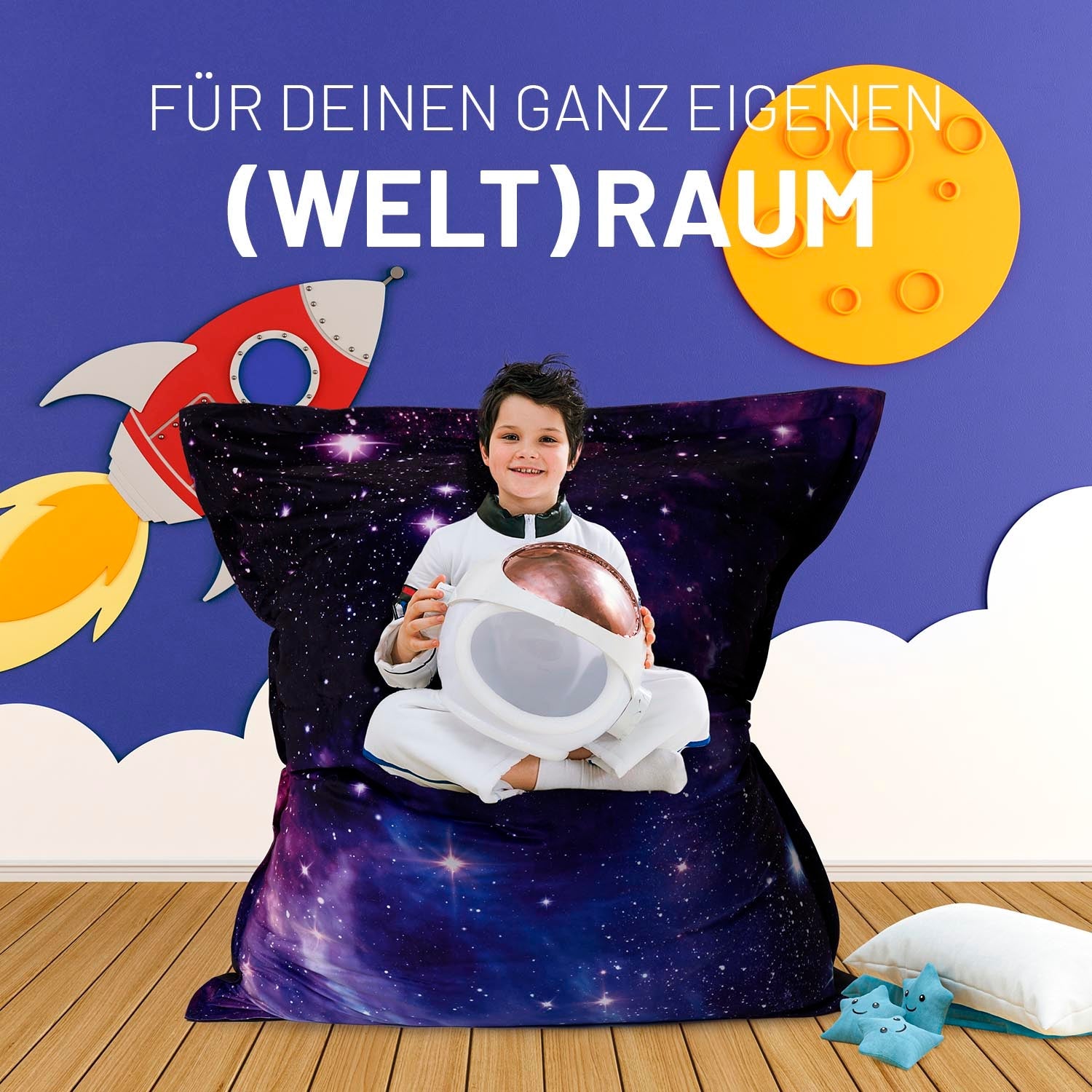 Ein kleiner Junge mit Raumfahreranzug und Helm sitzt auf dem Galaxy Sitzsack vor einer Wand mit Rakete und Mond.