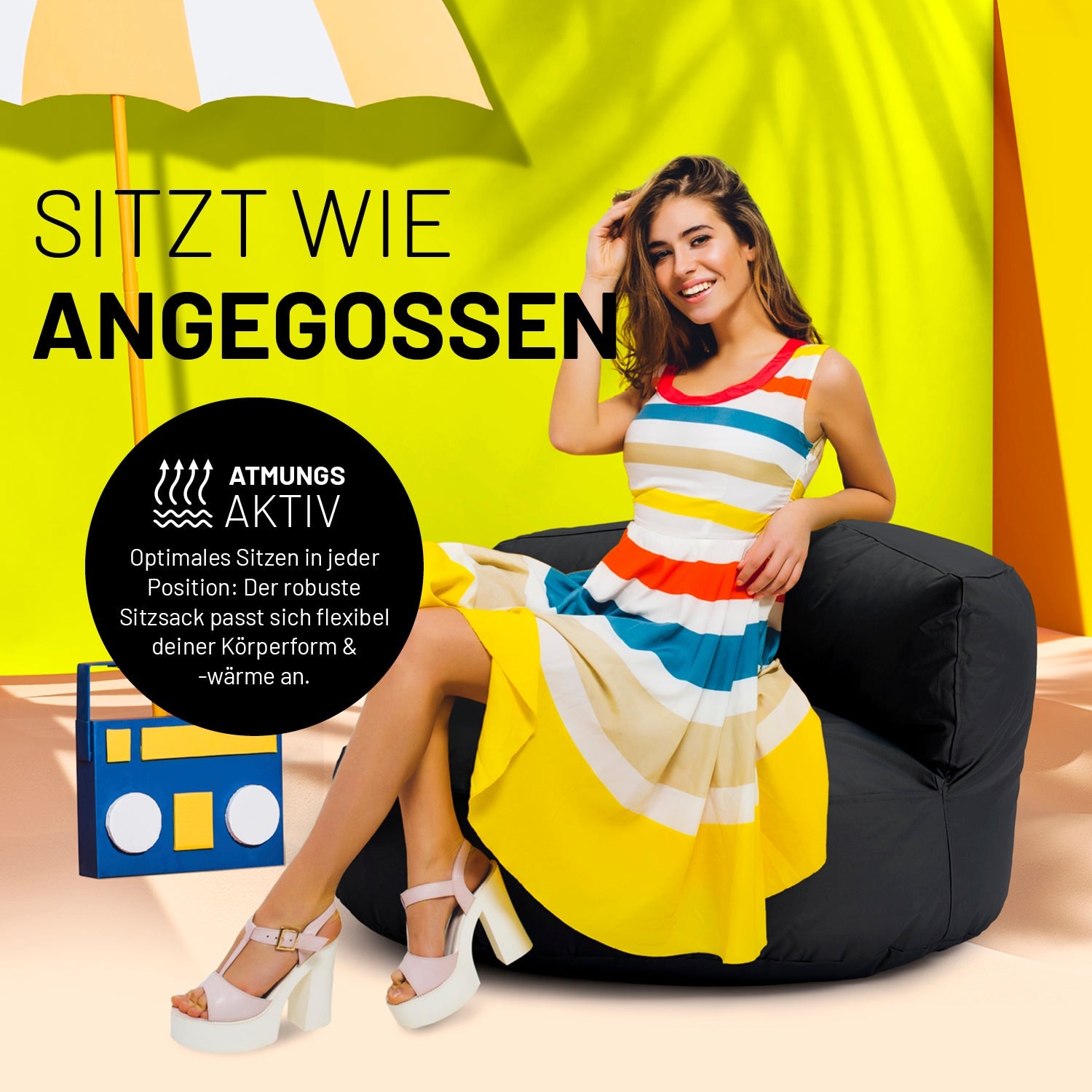Eine Frau in buntem Kleid sitzt auf dem schwarzen Sitzsack-Sofa. Icon "Atmungsaktiv" und "Passt sich Körperform und -wärme an".