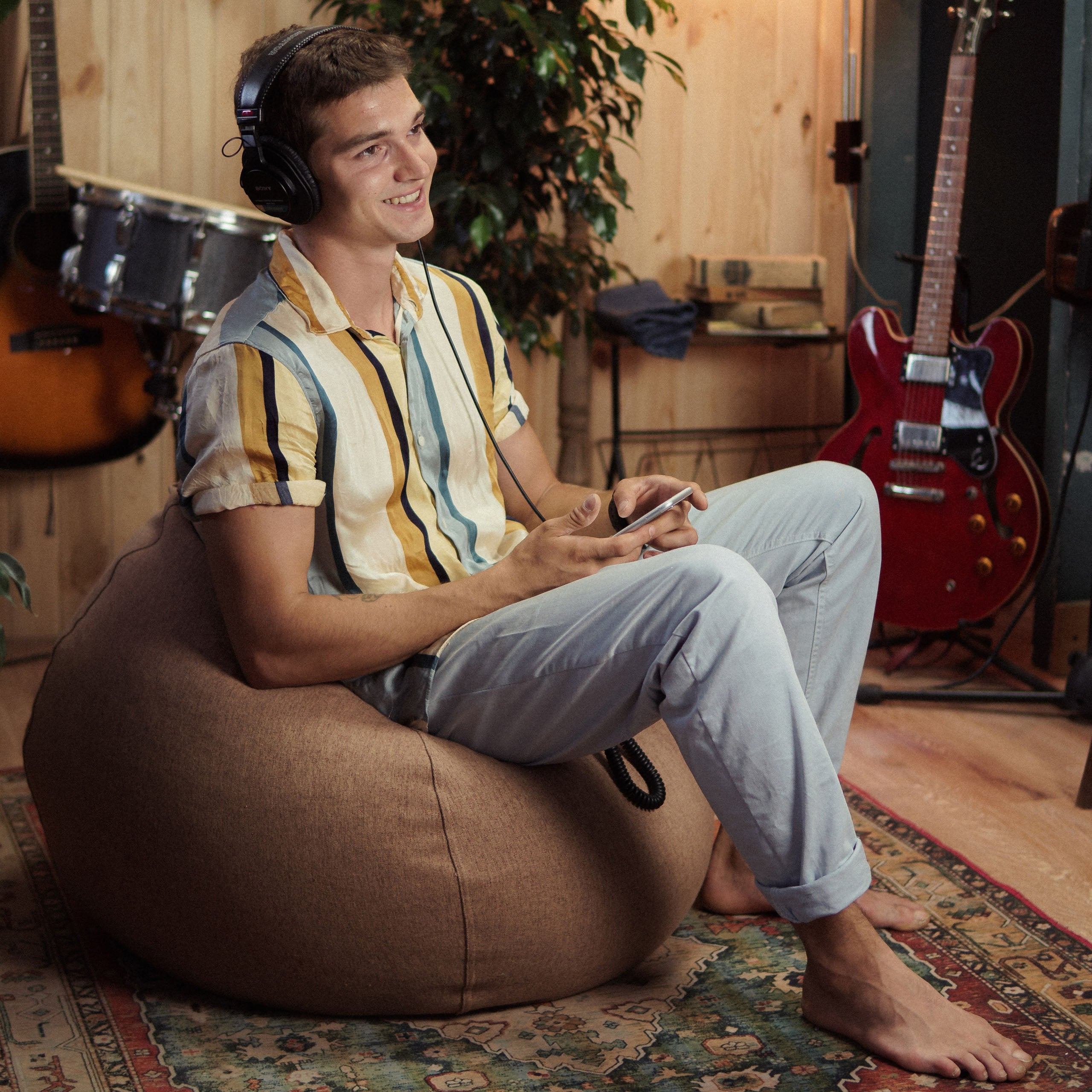 Ein Mann sitzt im Comfort Line Sitzsack in Braun und hört Musik, im Hintergrund Gitarren und Schlagzeug.