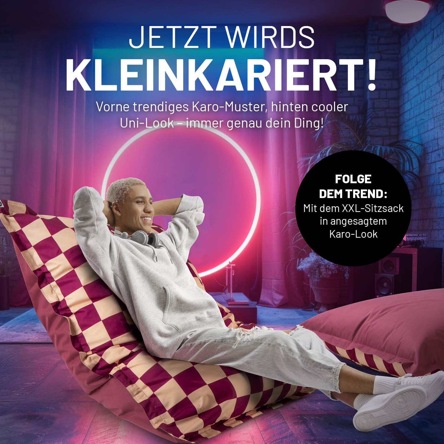 Ein Mann entspannt mit überkreuzten Beinen auf dem XXL-Sitzsack im trendigen Karo-Muster mit Uni-Look Rückseite. 