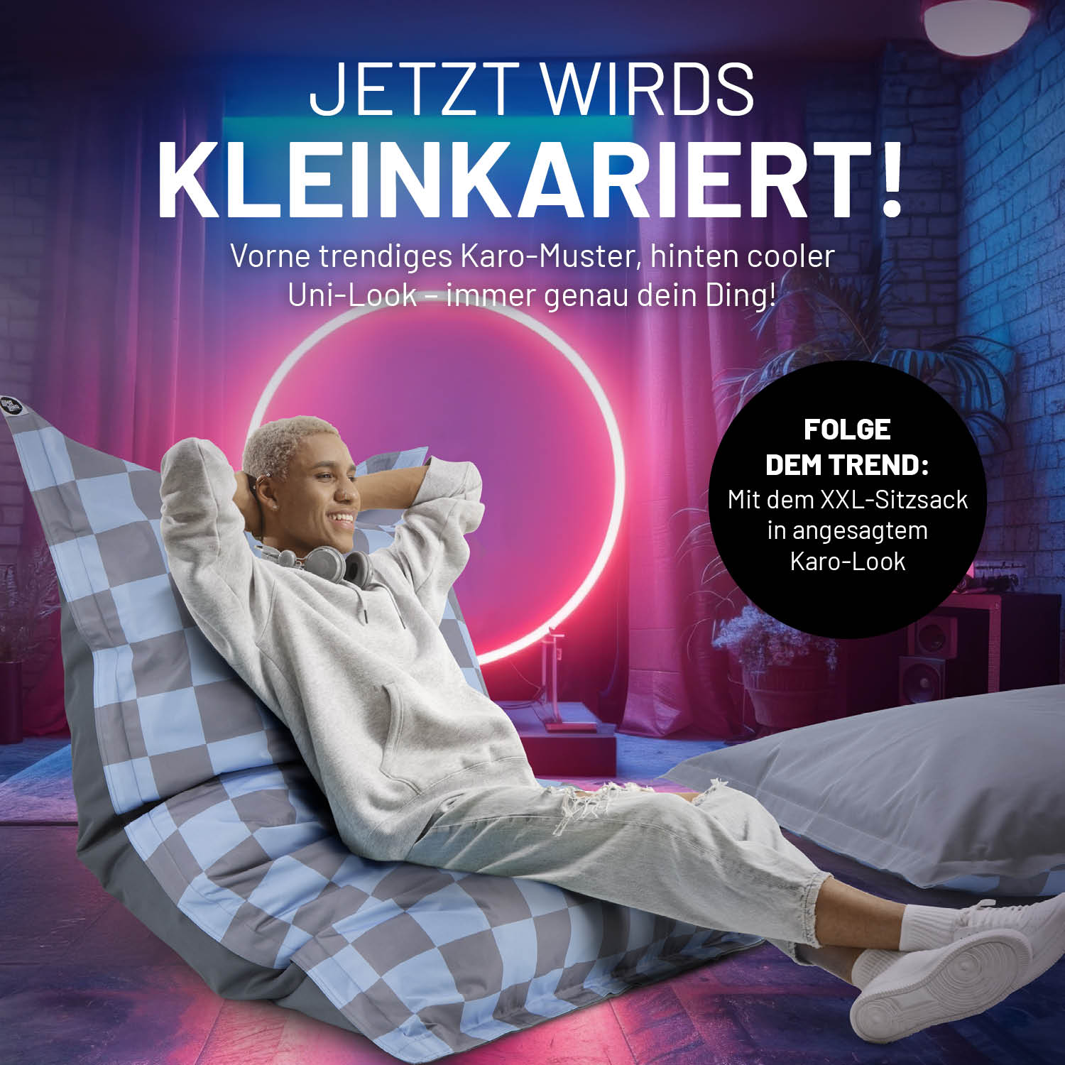 Ein Mann entspannt mit überkreuzten Beinen auf dem XXL-Sitzsack im trendigen Karo-Muster mit Uni-Look Rückseite. 