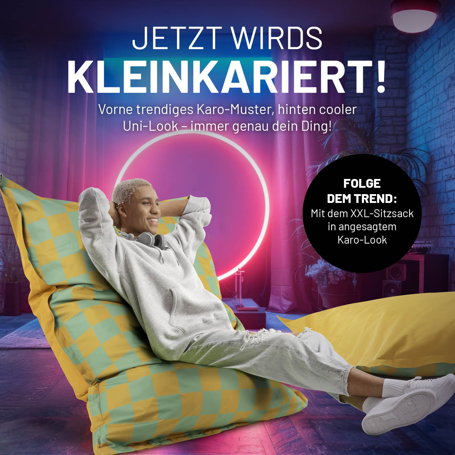 Ein Mann entspannt mit überkreuzten Beinen auf dem XXL-Sitzsack im trendigen Karo-Muster mit Uni-Look Rückseite. 